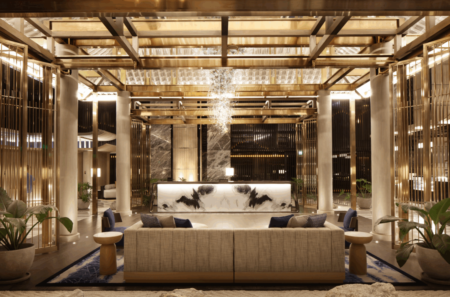 Luxurious hotel lobby with a marble front desk, elegant chandelier, plush seating, and gold accents. Warm, inviting atmosphere with a modern design.