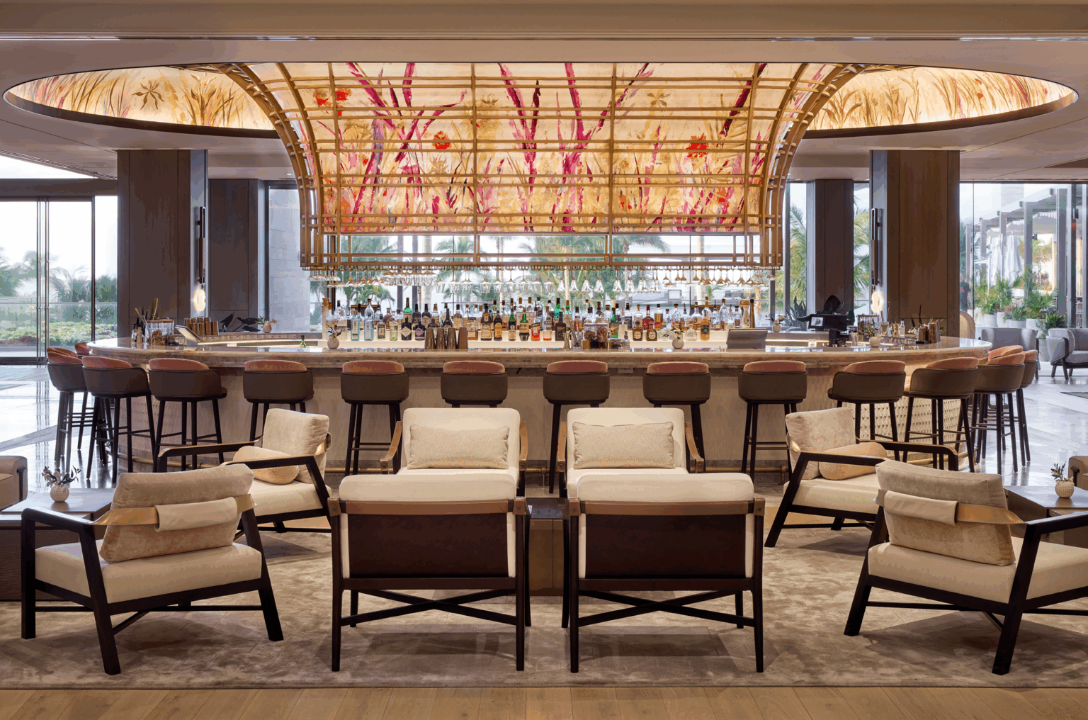 Luxurious hotel bar interior featuring a large, illuminated floral ceiling, surrounded by plush chairs and stools, creating a welcoming and elegant ambiance.