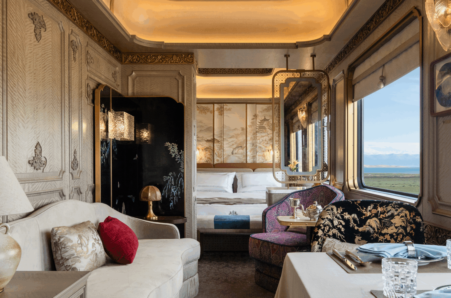 Luxurious train cabin with elegant decor, featuring ornate paneling, plush seating, a cozy bed, soft lighting, and scenic window view of rolling fields.