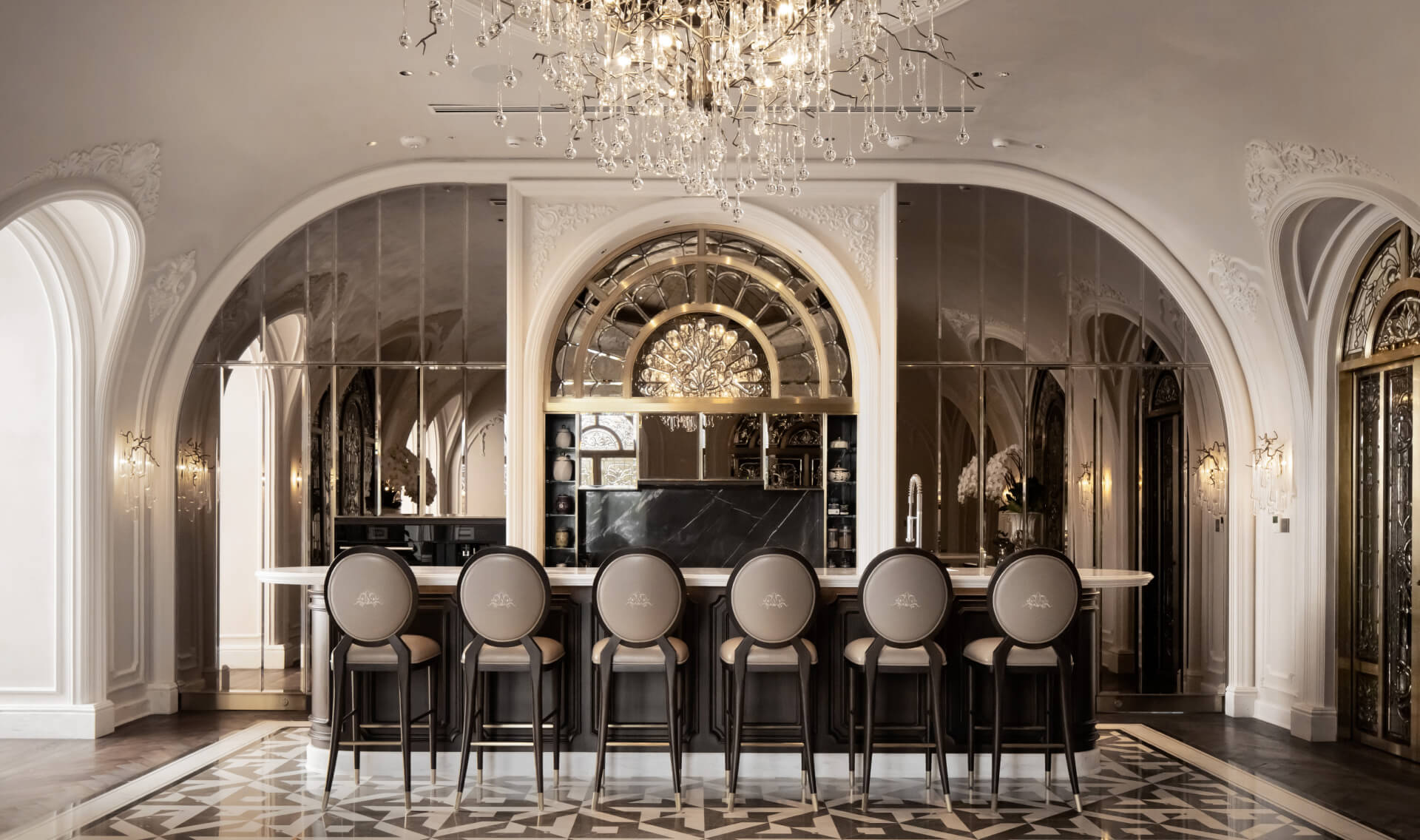 Elegant bar with arched mirrors, a crystal chandelier, and six high-back stools. Luxurious, classic decor with intricate details and warm lighting.