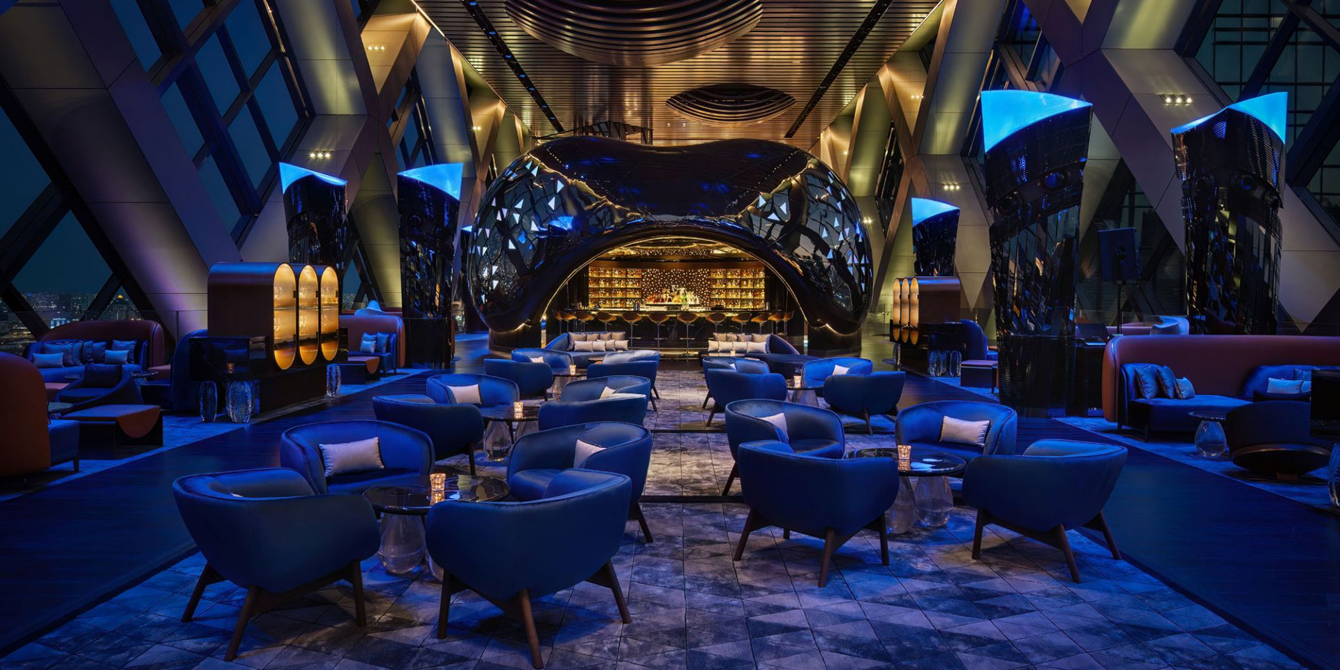 Luxurious bar lounge area with futuristic design, featuring blue-lit seating, modern architecture, and a sleek bar. The ambiance is elegant and inviting.