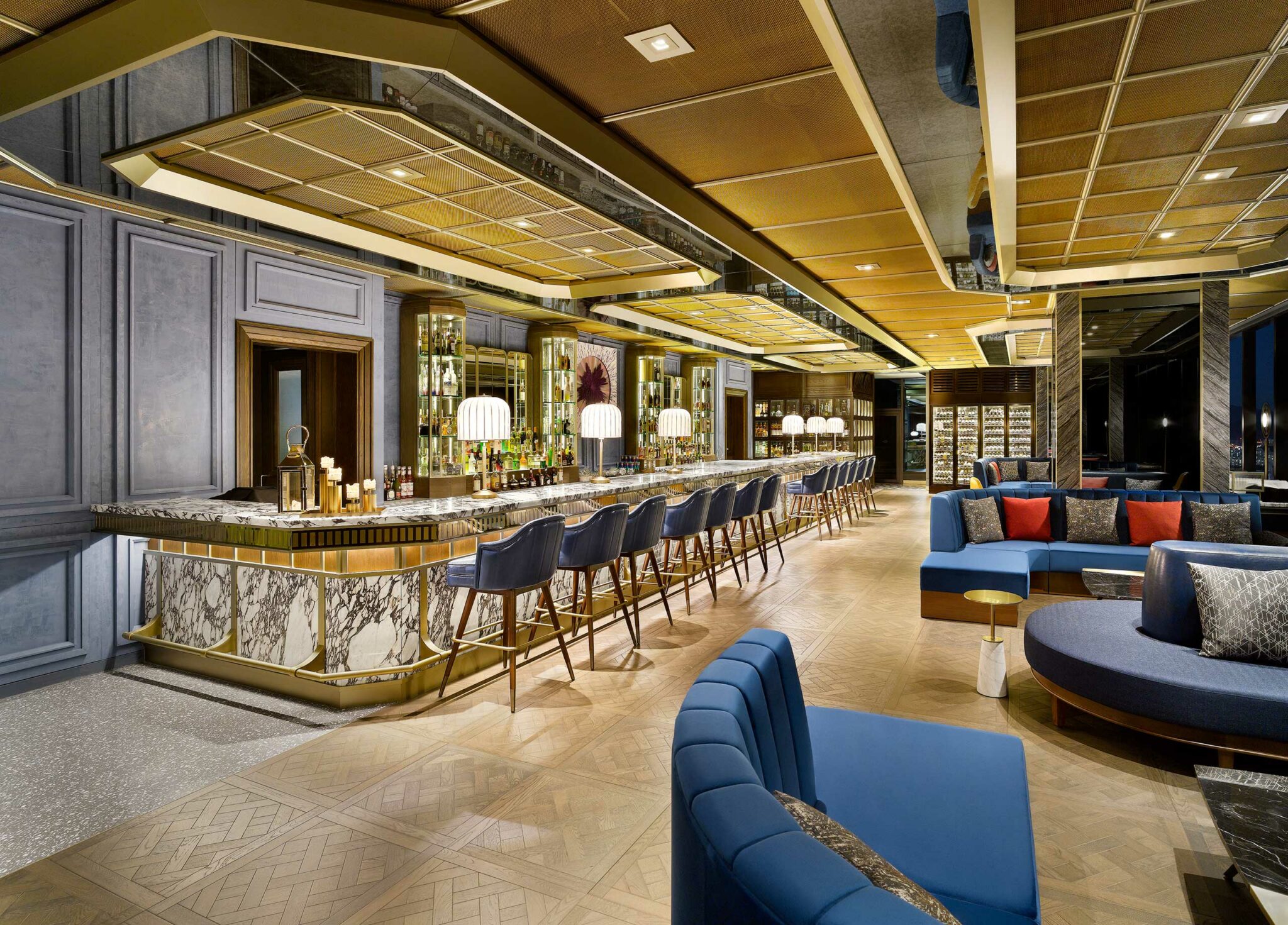 Luxurious hotel bar interior with a long marble counter and blue stools. Soft lighting, golden accents, and blue seating create an elegant, inviting ambiance.