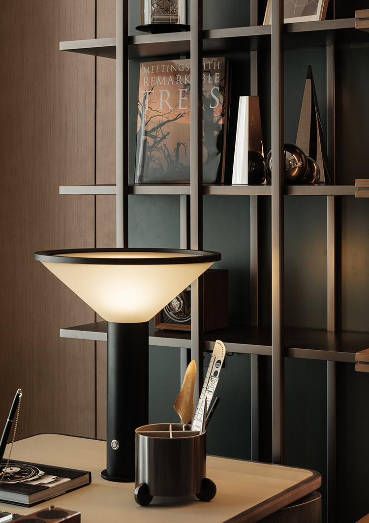 A stylish desk setup featuring a modern lamp, a sleek container for utensils, and a bookshelf with decorative items and books, creating a sophisticated and functional workspace.