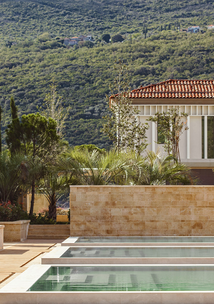 Luxurious villa with terracotta roof, palm trees, and a serene infinity pool in the foreground. Backdrop of lush green hills, evoking tranquility.