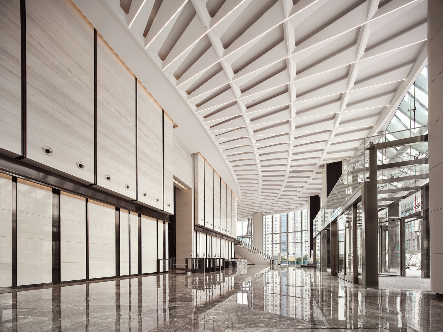 Spacious modern office lobby with geometric ceiling patterns, sleek marble floors, and a minimalist reception desk, conveying a sophisticated and elegant tone.