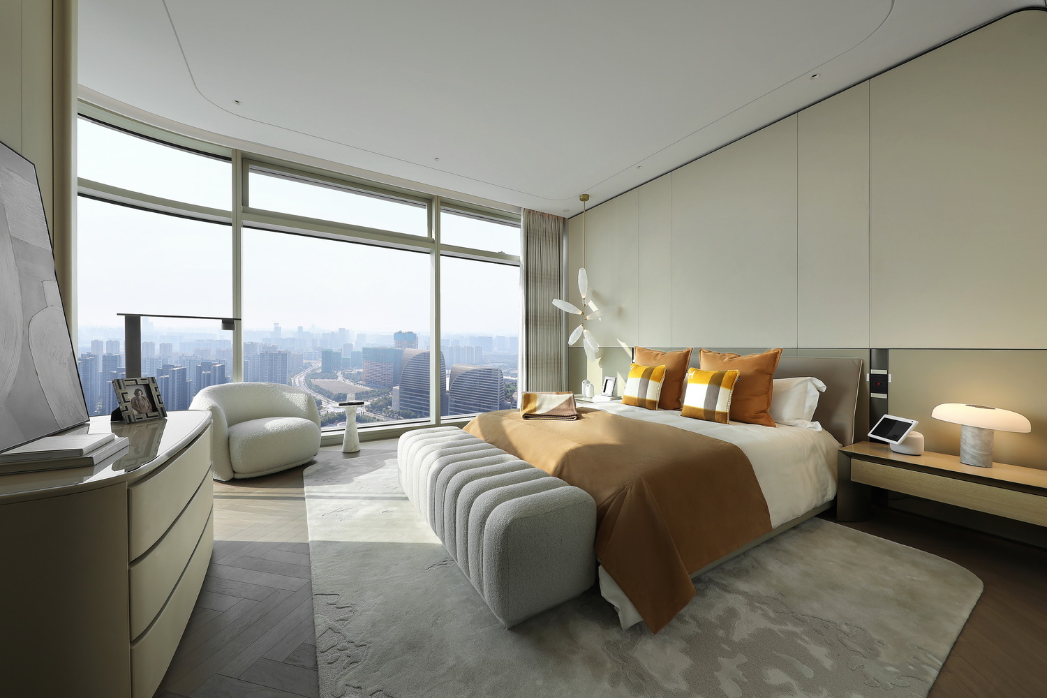 Modern bedroom with a cozy beige bed, two plaid pillows, and a plush bench at the foot. Sunlight streams through a large window, enhancing warmth.