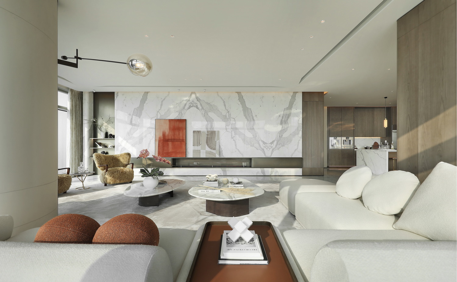 A modern living room with large windows, sunlight streaming in. Features include a plush chair, abstract wall art, round table, and curved sofa. The ambiance is serene and sophisticated.