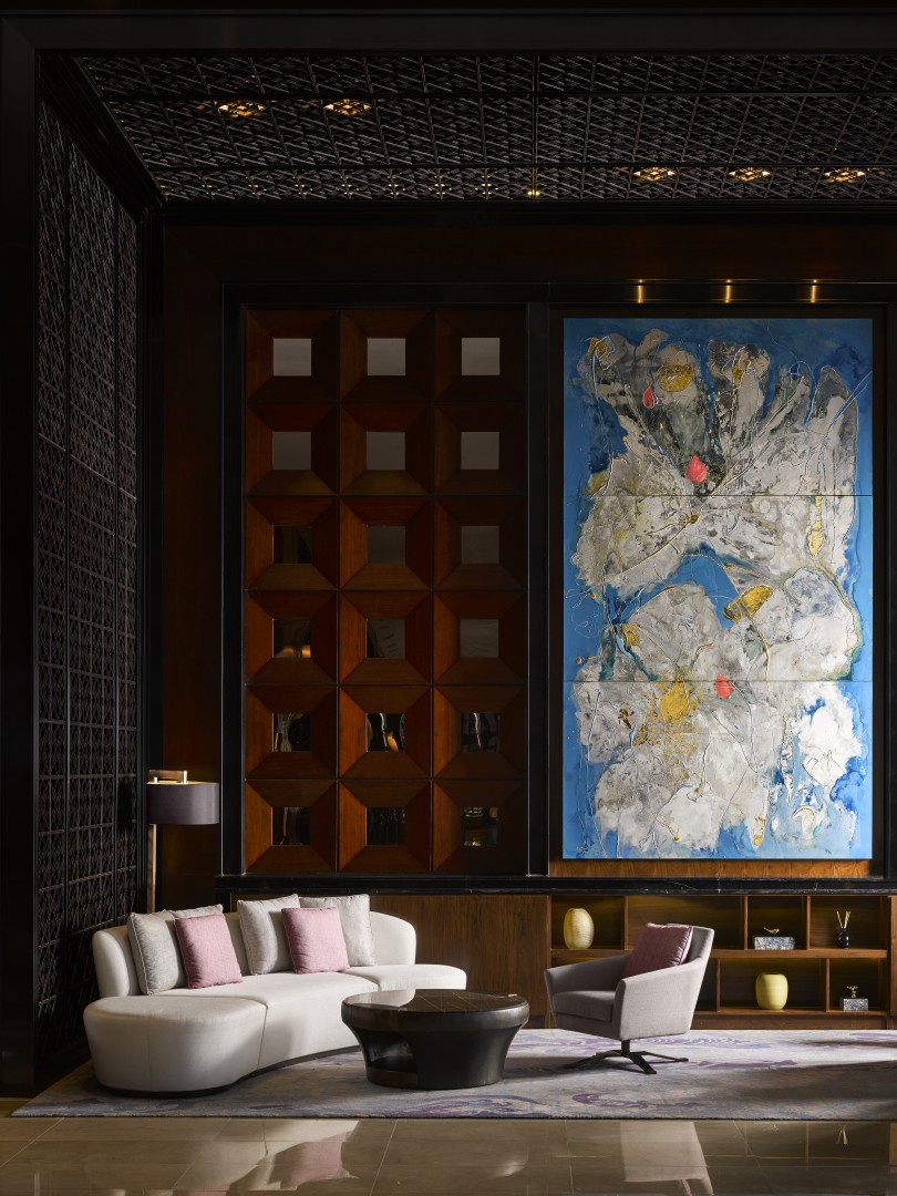 Hotel lounge with contemporary white sofa, armchair, geometric wood wall panels, and large abstract artwork.