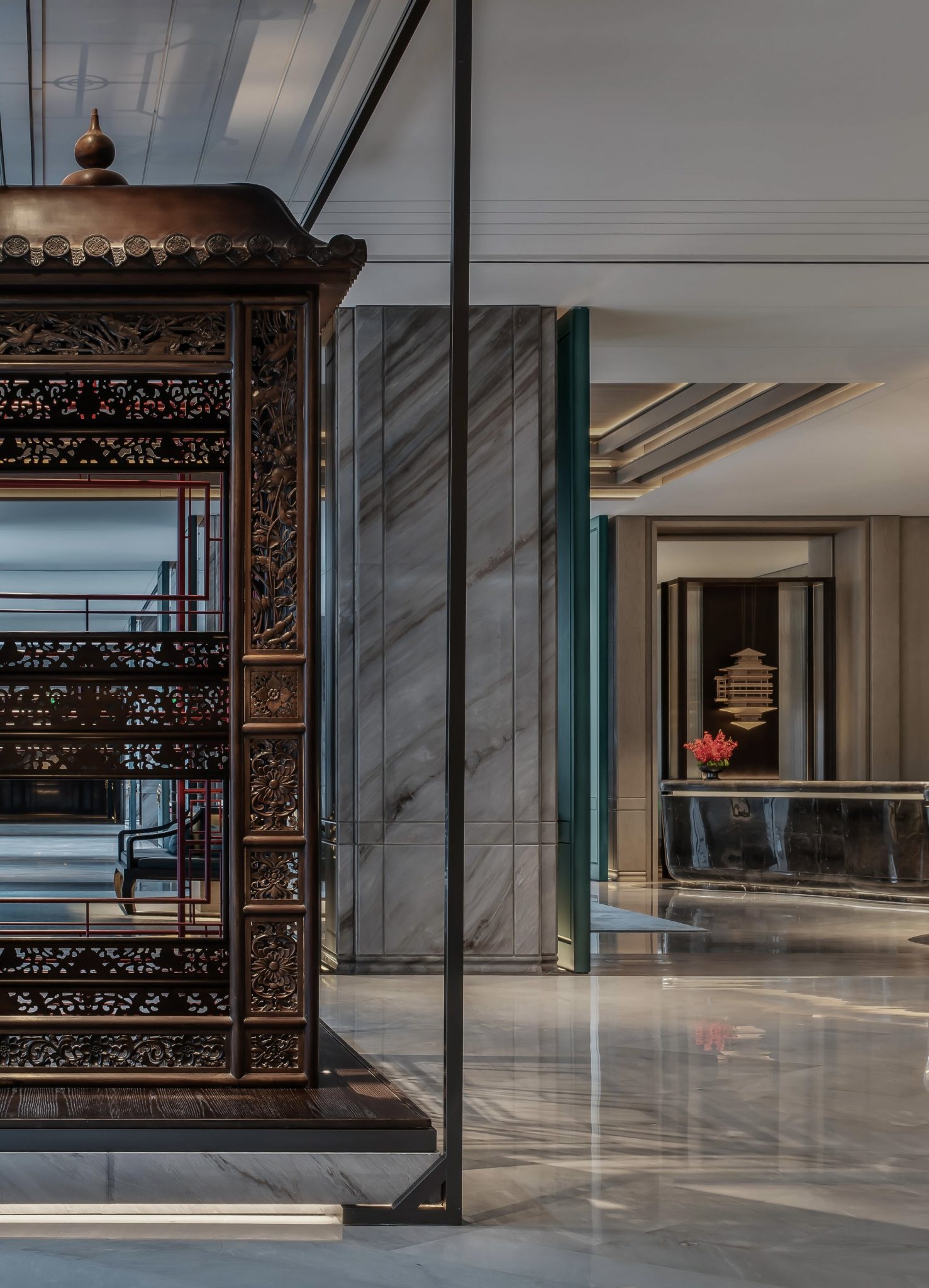 Hotel corridor featuring an intricately carved wooden pavilion structure, framed by marble walls and teal double doors.