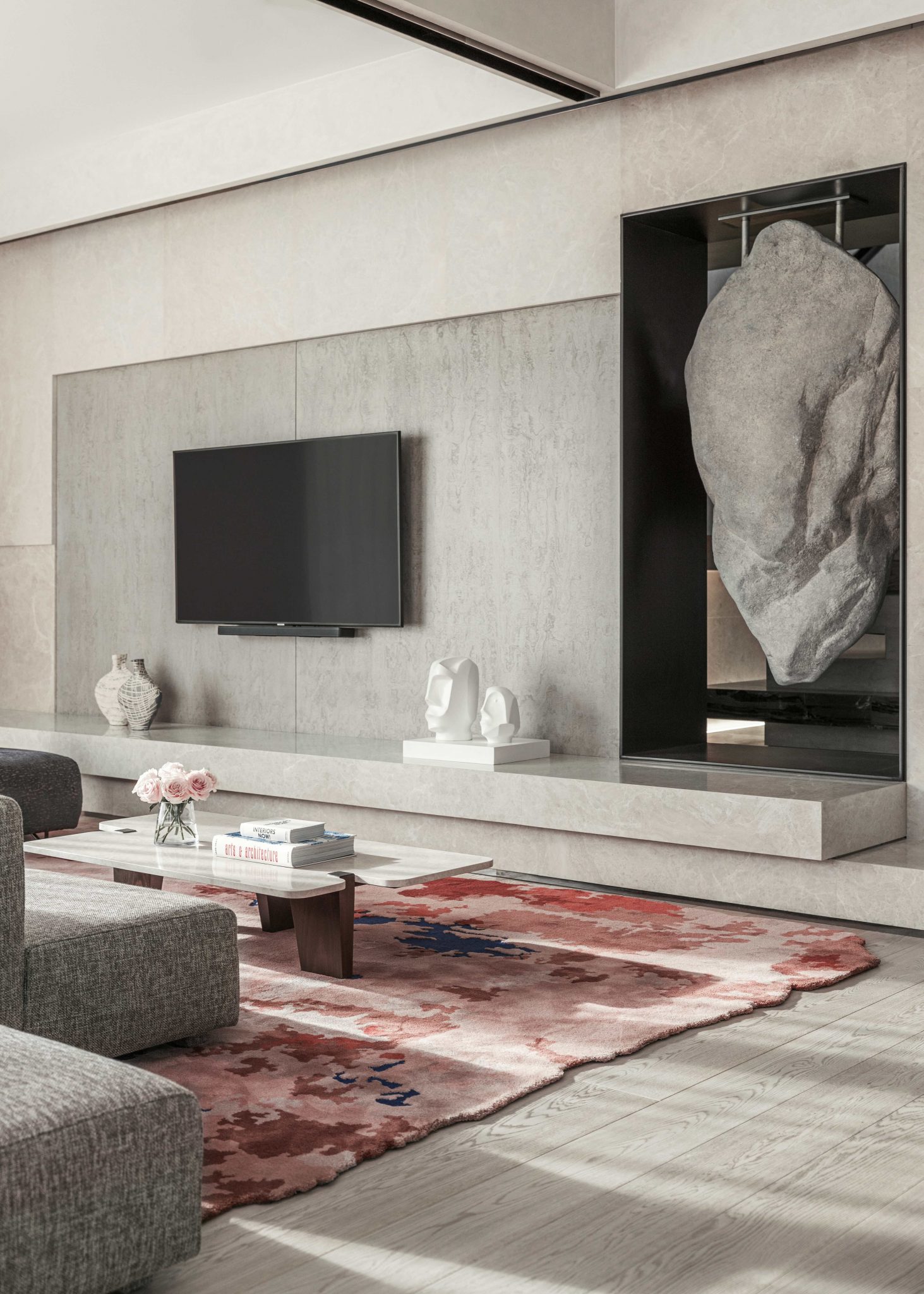 Modern living space with a suspended stone sculpture, abstract red patterned rug, and minimalist wall-mounted TV.