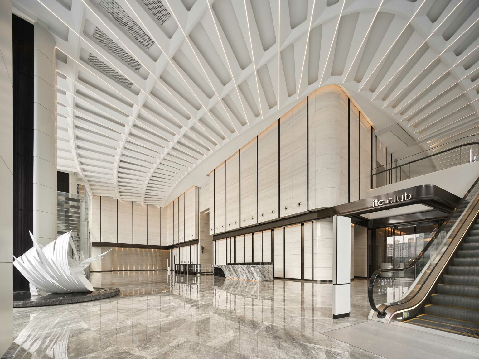 Spacious office lobby with high ceilings and geometric design, featuring a white abstract sculpture on glossy marble floors, adjacent to an escalator and modern decor.