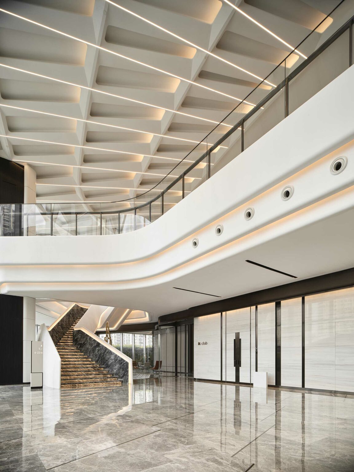 Modern, spacious office lobby with sleek marble floors and a grand staircase. Geometric ceiling and soft lighting create a minimalist, elegant atmosphere.