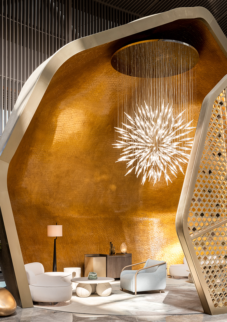 A striking hotel lounge area featuring a golden, sculptural wall, a unique starburst chandelier, and contemporary seating, creating a luxurious and artistic atmosphere for relaxation and social interaction.