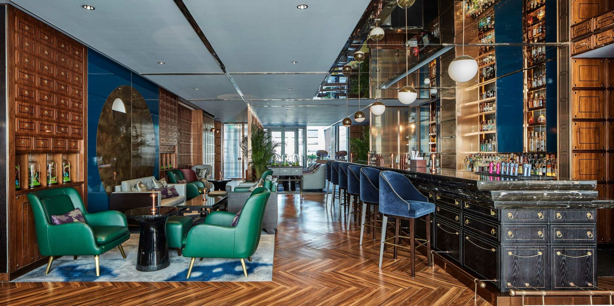 Luxurious hotel bar lounge with velvet green chairs, navy bar stools, wood paneling, mirrored walls, and ambient lighting, creating an elegant and cozy atmosphere.