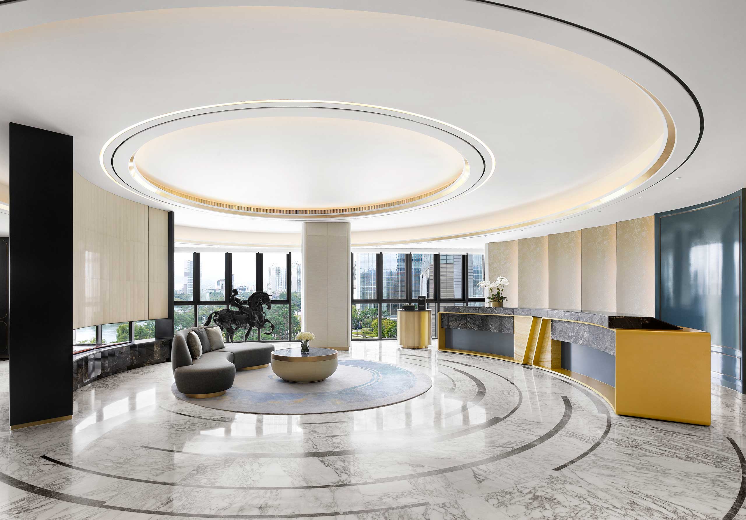Sophisticated hotel lobby with a circular ceiling design, modern seating, and a horse statue. Large windows reveal a cityscape, evoking elegance and grandeur.