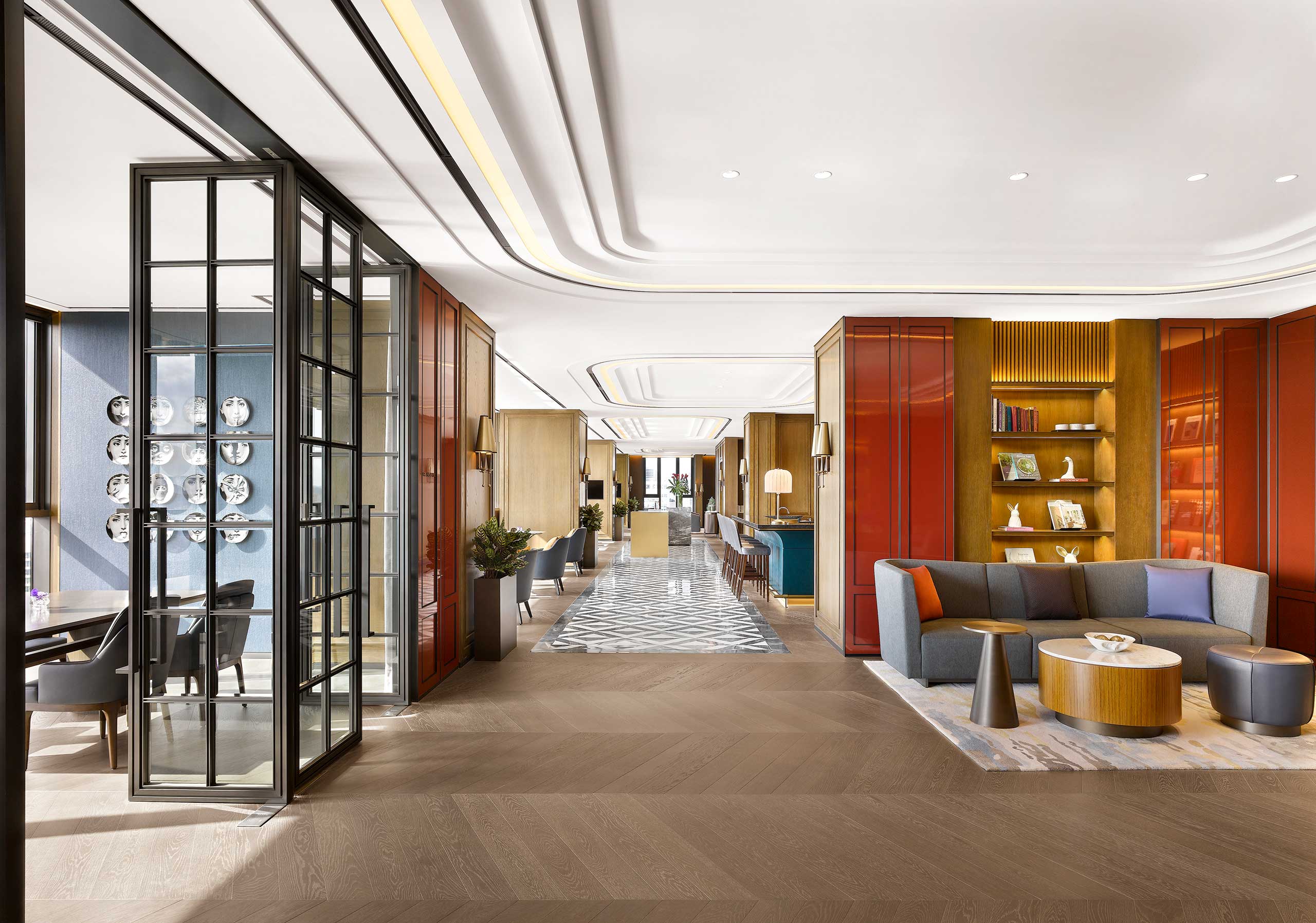 Modern hotel lobby with elegant design, featuring a cozy seating area with a gray sofa, wooden tables, and bookshelves. Bright and spacious ambiance.