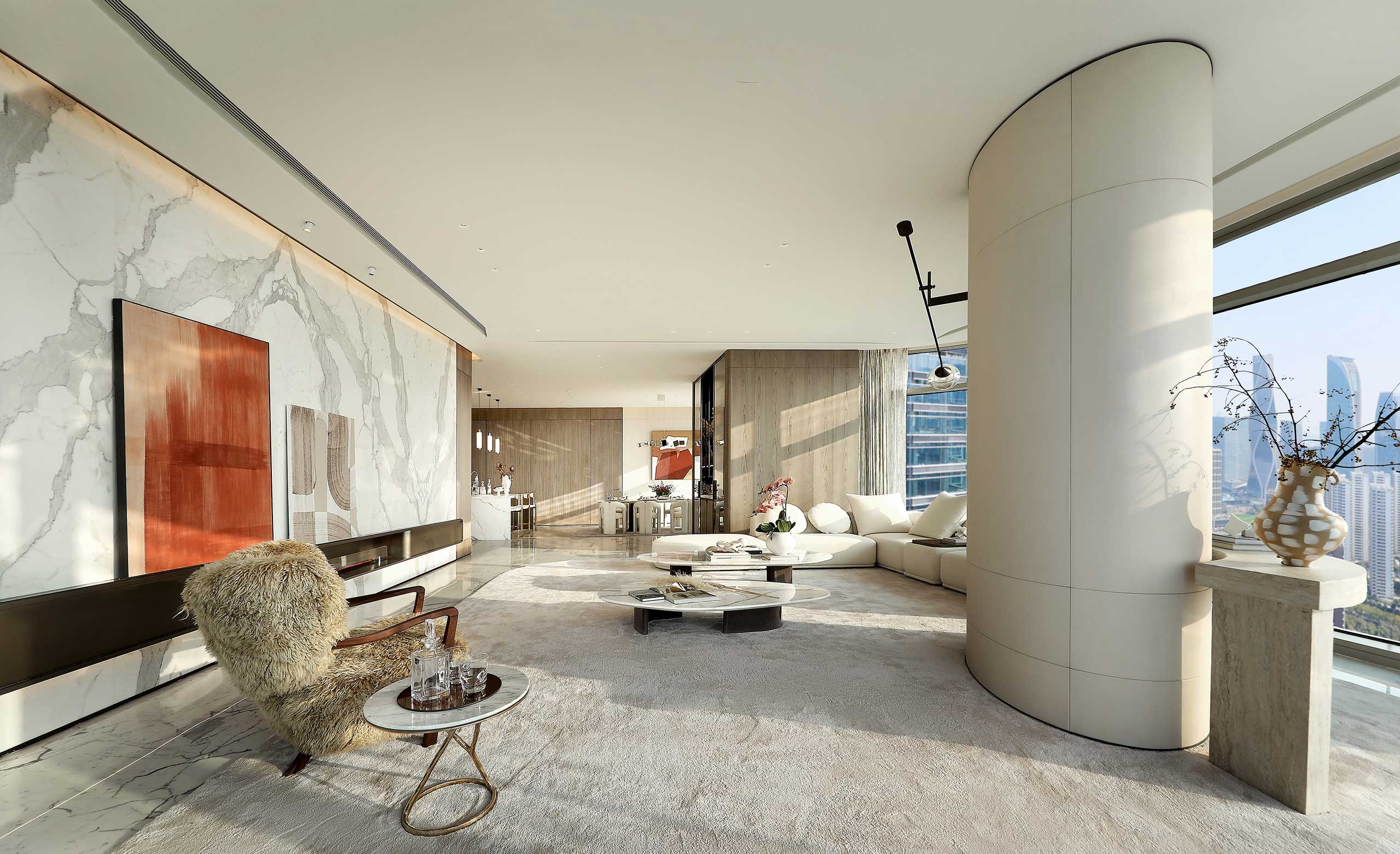 A modern living room with large windows, sunlight streaming in. Features include a plush chair, abstract wall art, round table, and curved sofa. The ambiance is serene and sophisticated.