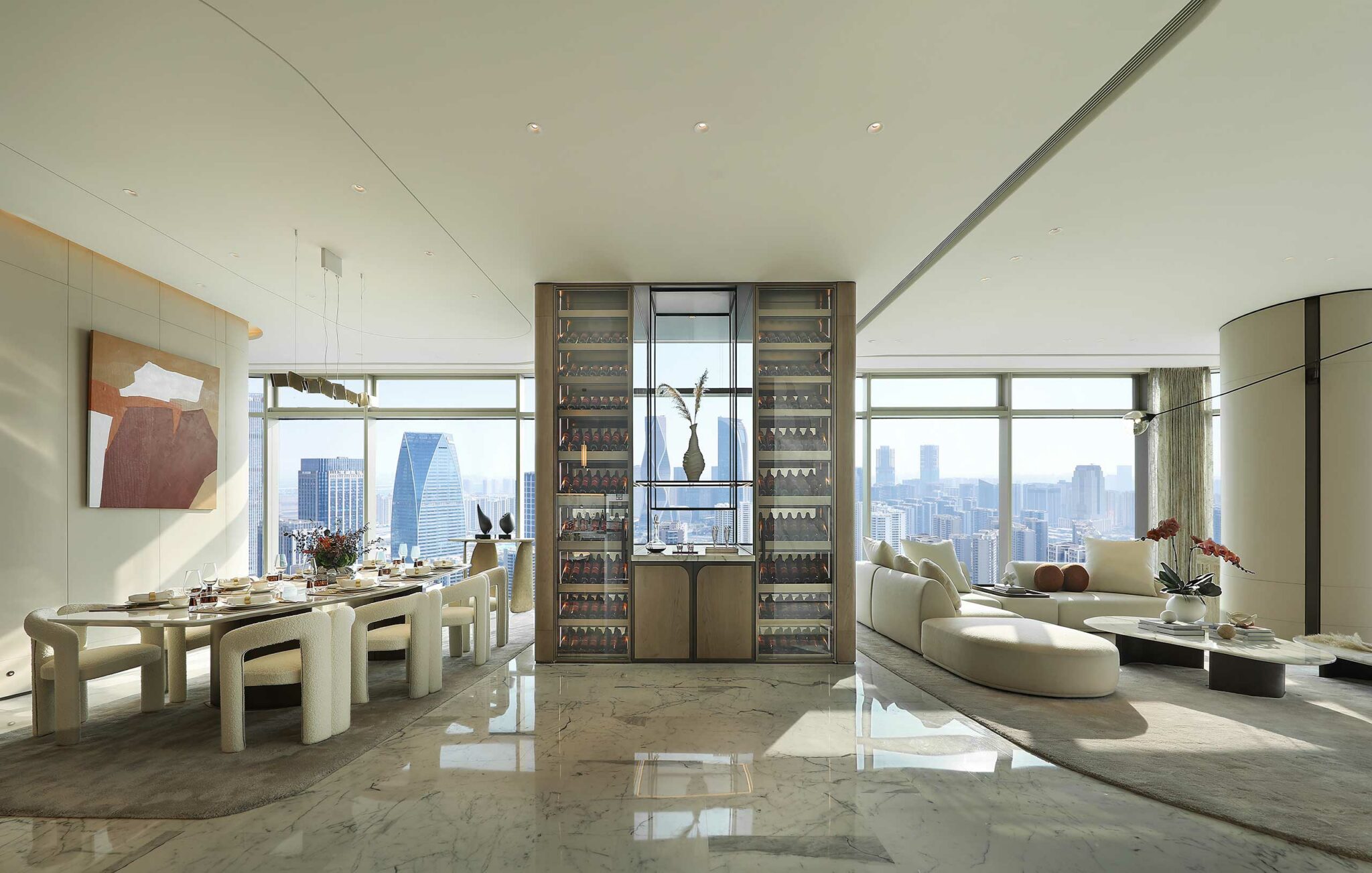 Luxurious modern living and dining area with marble floors, showcasing a panoramic city view. Elegant furniture, art, and wine display add sophistication.