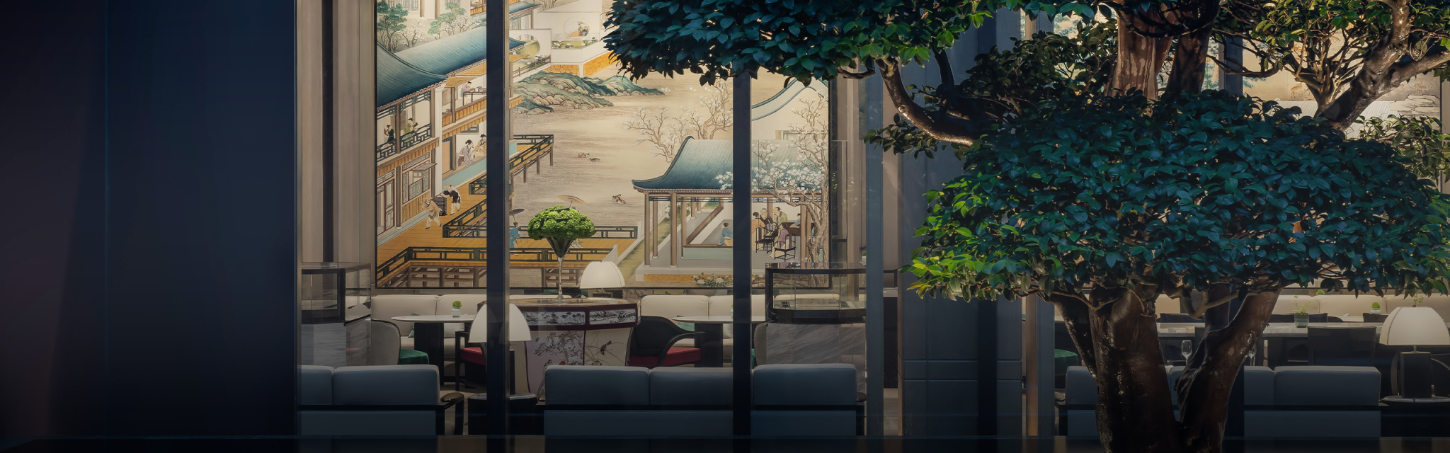 Modern hotel lounge with minimalist decor viewed through large windows. A mural of traditional Asian architecture is visible inside, with lush green trees outside.