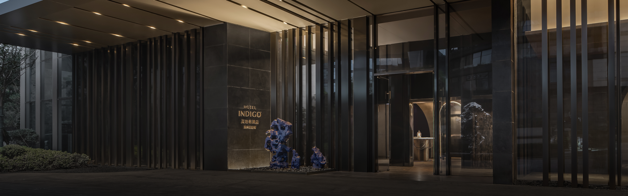Modern hotel entrance featuring a sleek, minimalist design with dark panels and vertical lines. Blue sculptures add a bold contrast, creating a sophisticated ambiance.