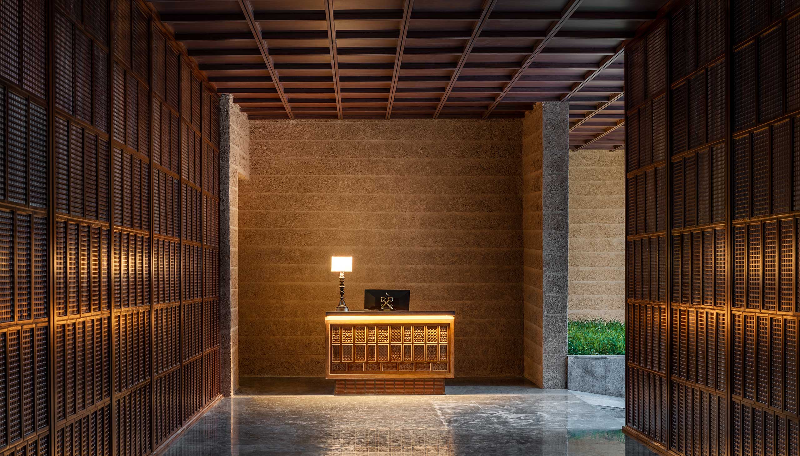 A warmly lit hotel reception area with a wooden desk, decorative paneling, and a glowing lamp. The minimalist design exudes a calm and welcoming atmosphere.
