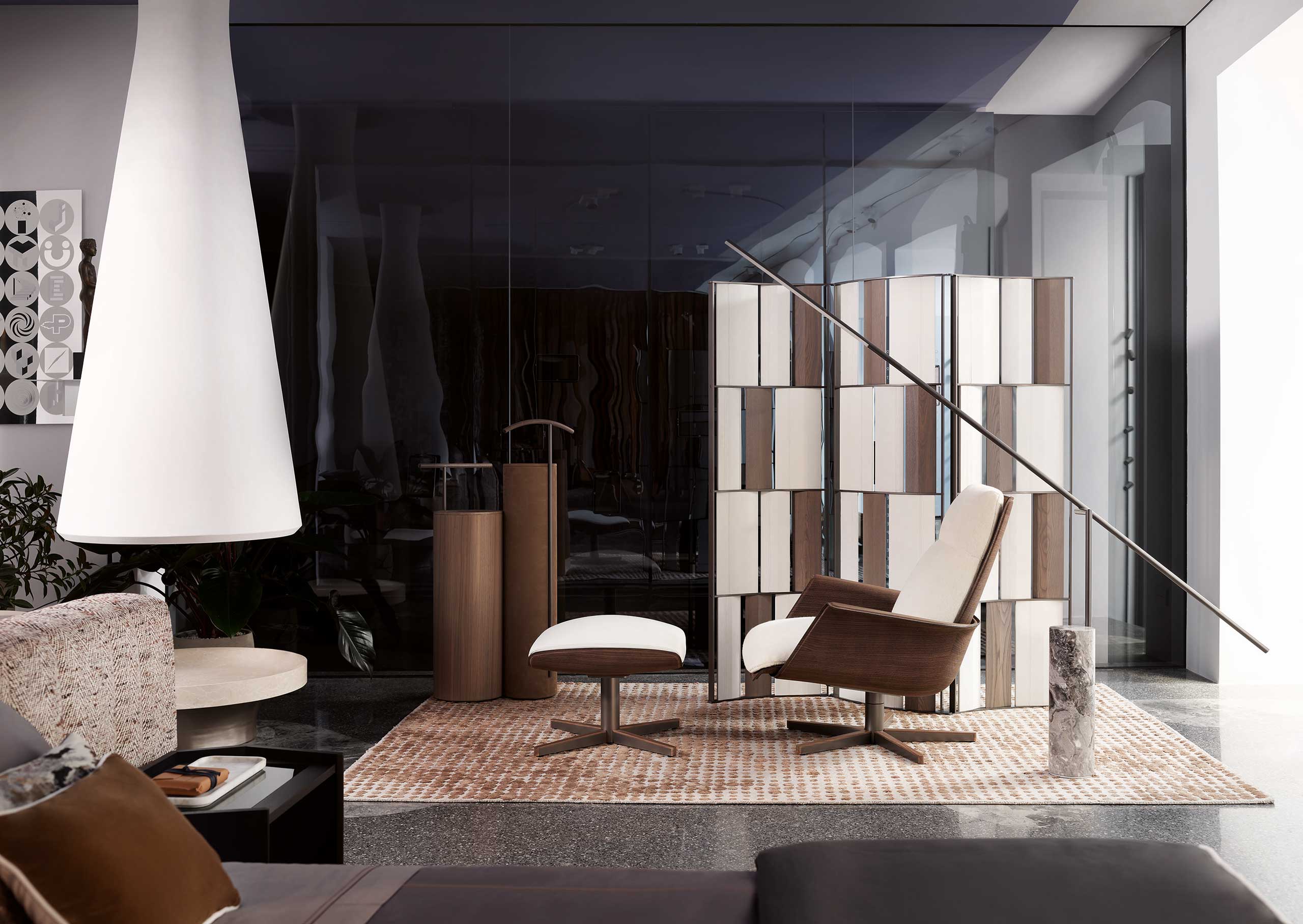 Modern living room with a dark glass wall, white cone-shaped lamp, brown and cream lounge chair with matching ottoman, and geometric screen divider.