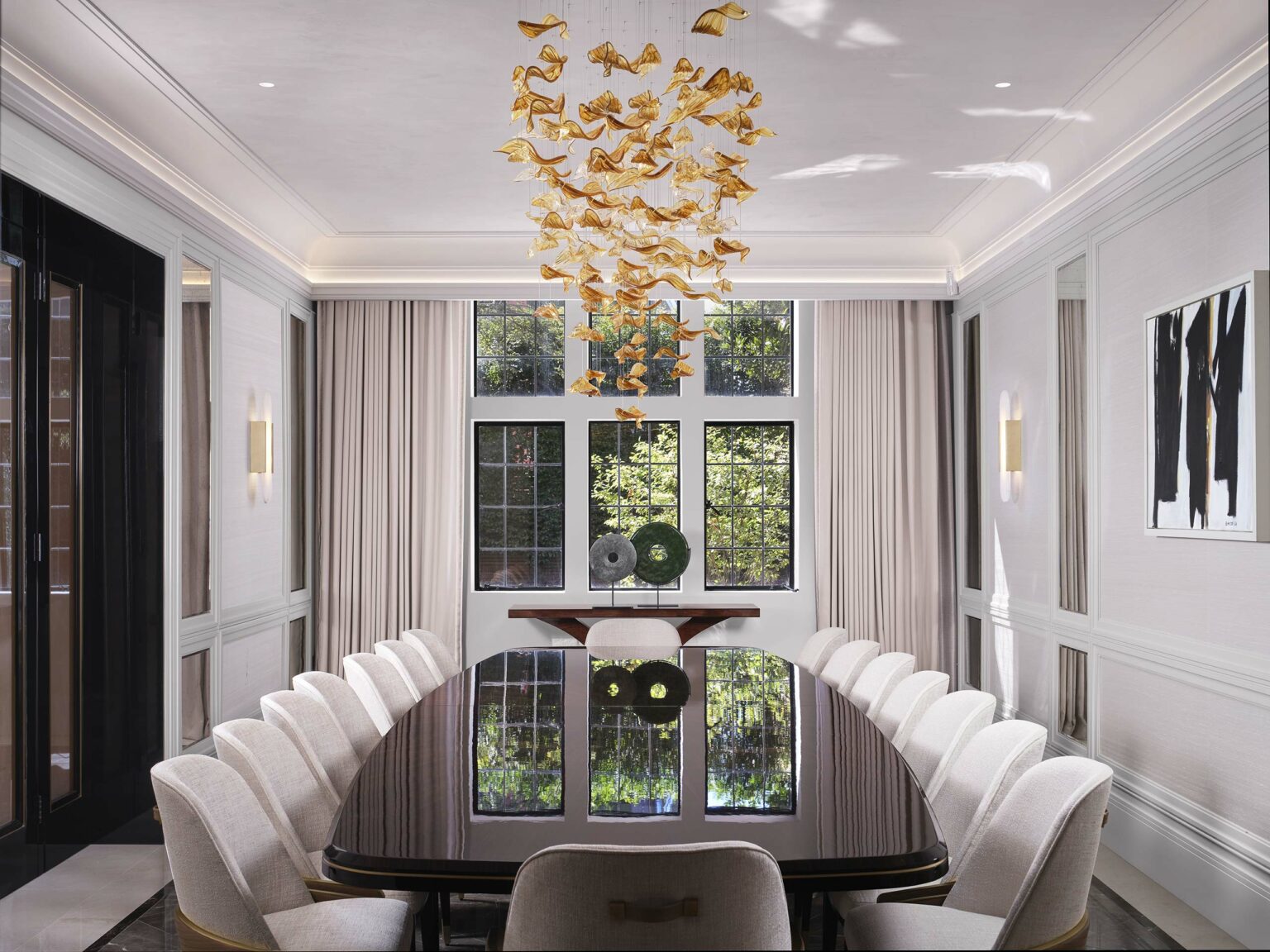 Luxurious dining room with a glossy black oval table surrounded by white chairs. A gold bird-shaped chandelier hangs above. Large windows with beige curtains reveal greenery outside, adding elegance.