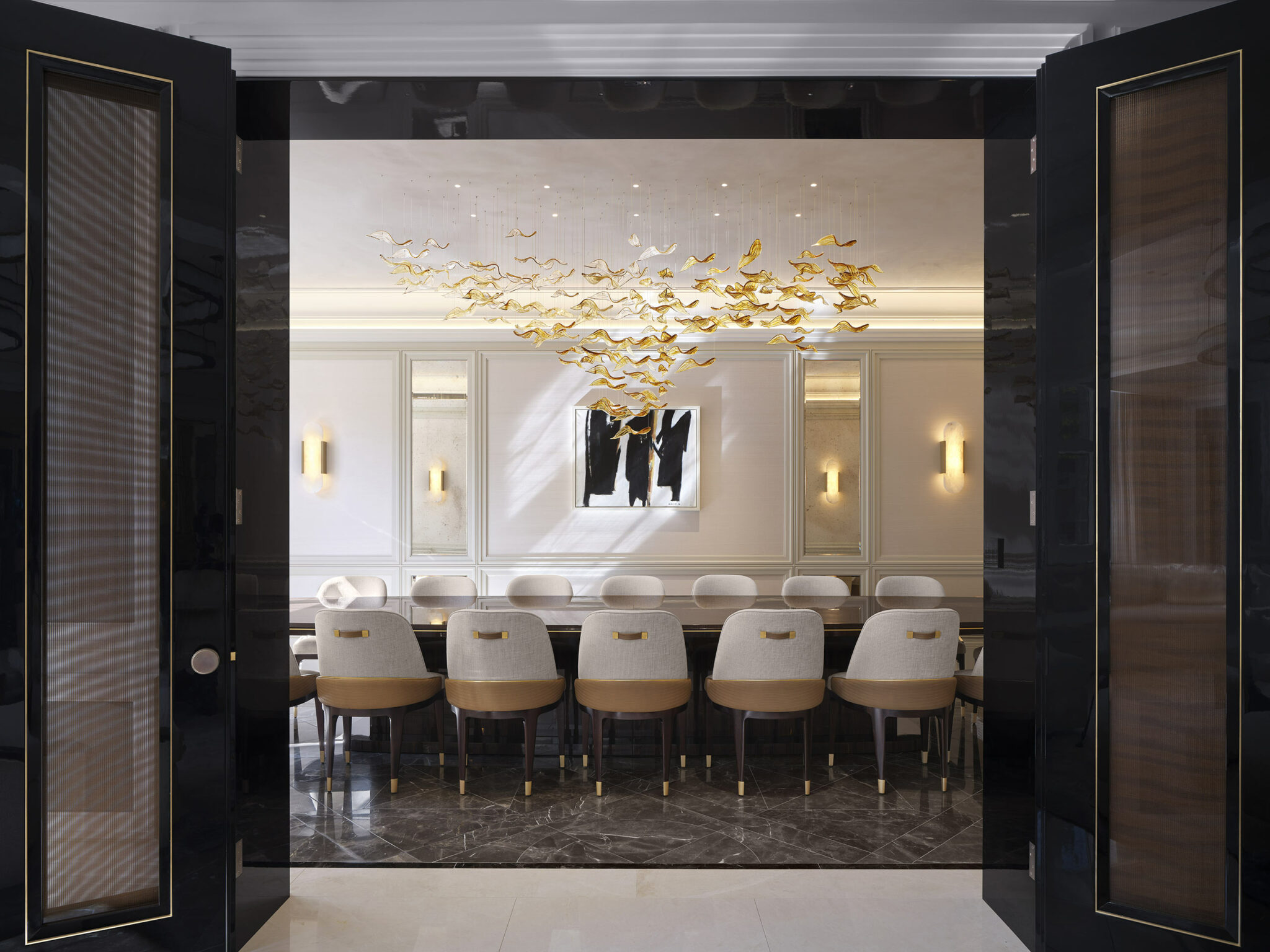 A luxurious dining room with a long table and elegant chairs. Above, an artistic golden chandelier resembling birds in flight adds sophistication.