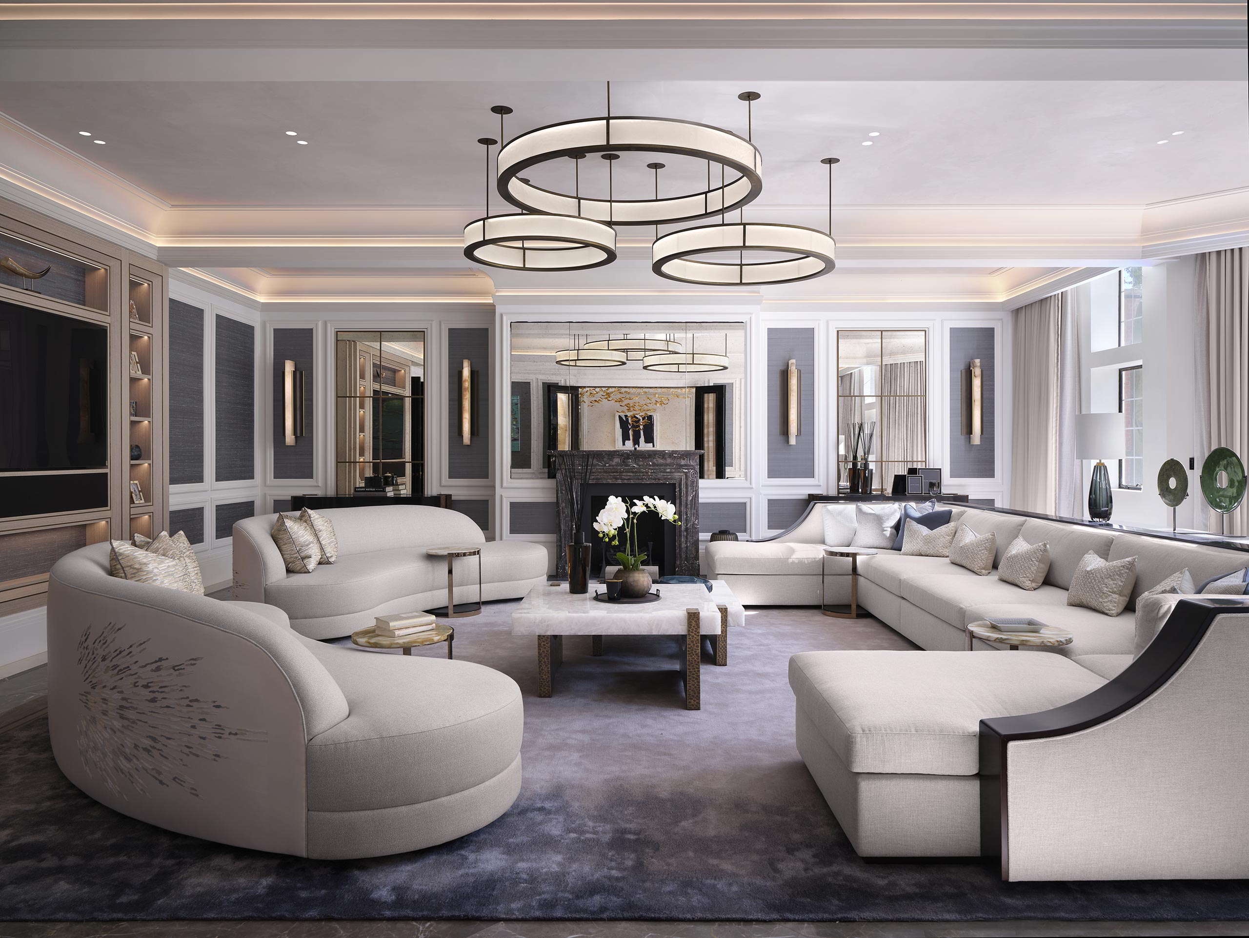 Elegant living room with gray sofas, circular chandeliers, and a marble fireplace. Soft lighting and neutral tones create a sophisticated, cozy atmosphere.