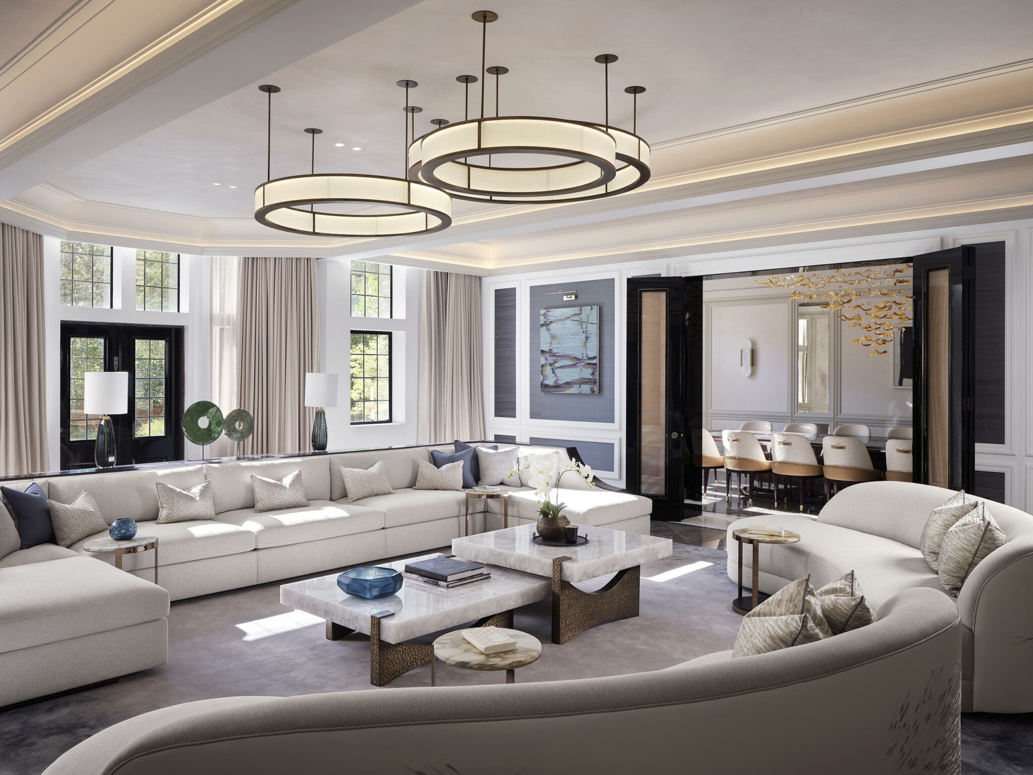 Luxurious living room with large beige sectional sofas, modern coffee tables, circular ceiling lights, and tall windows. Chic, spacious, and elegant atmosphere.