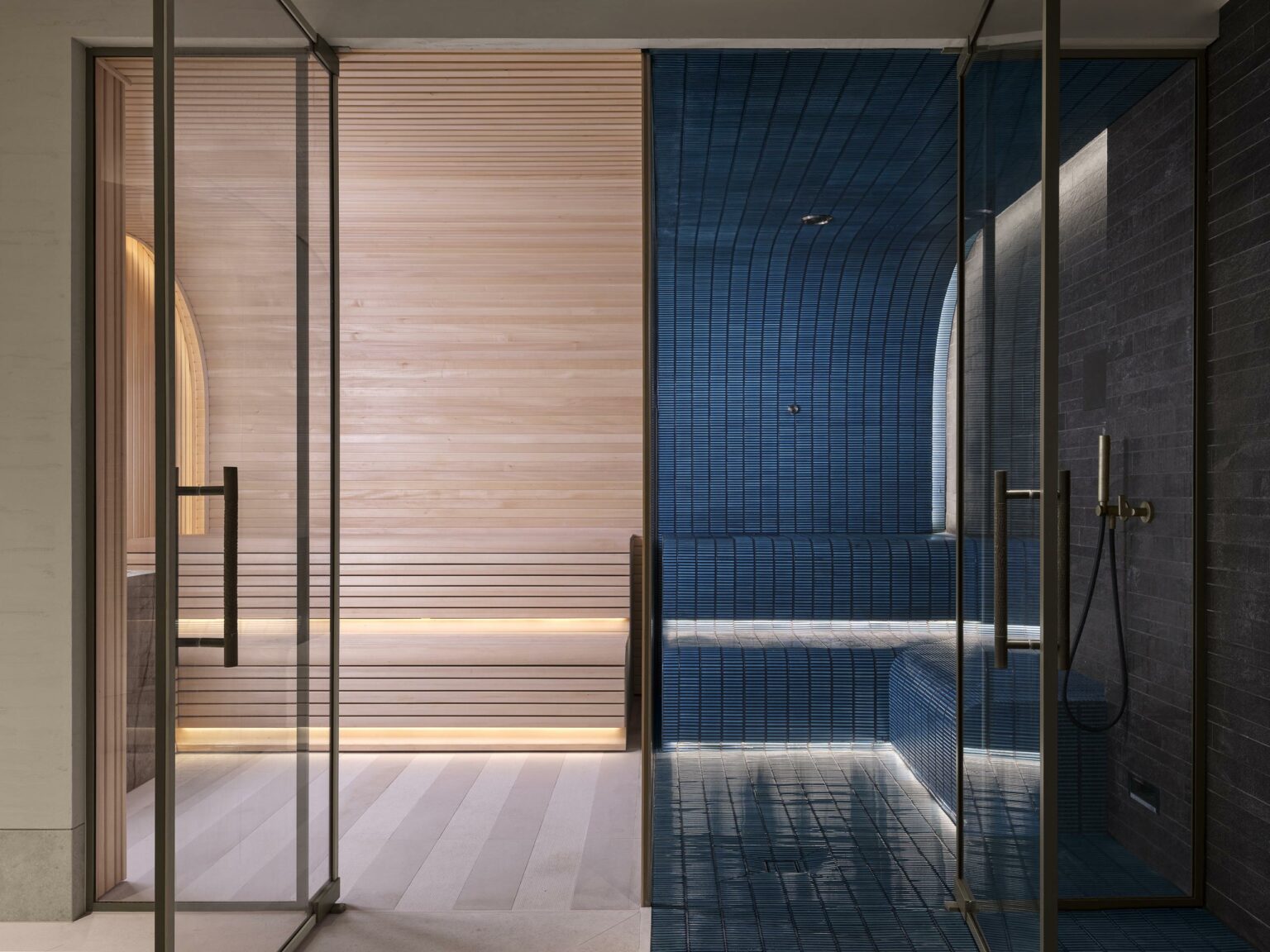 Luxurious private pool with adjoining rooms: a warm-toned wooden sauna on the left and a sleek, blue-tiled steam room on the right, both behind glass doors.