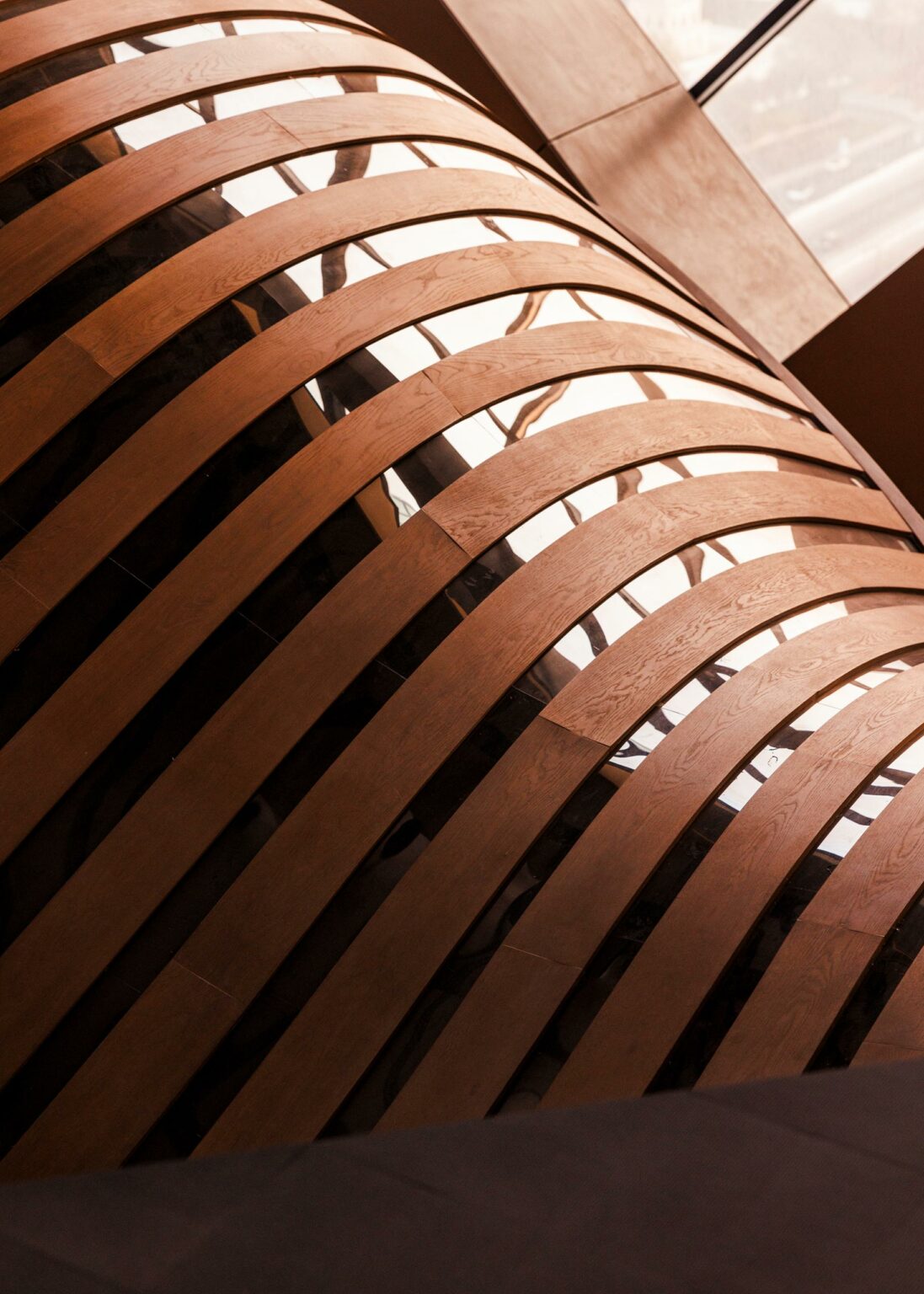 Curved wooden slats form a lattice pattern, casting shadows on a smooth, reflective glass surface. The design is modern and architectural.