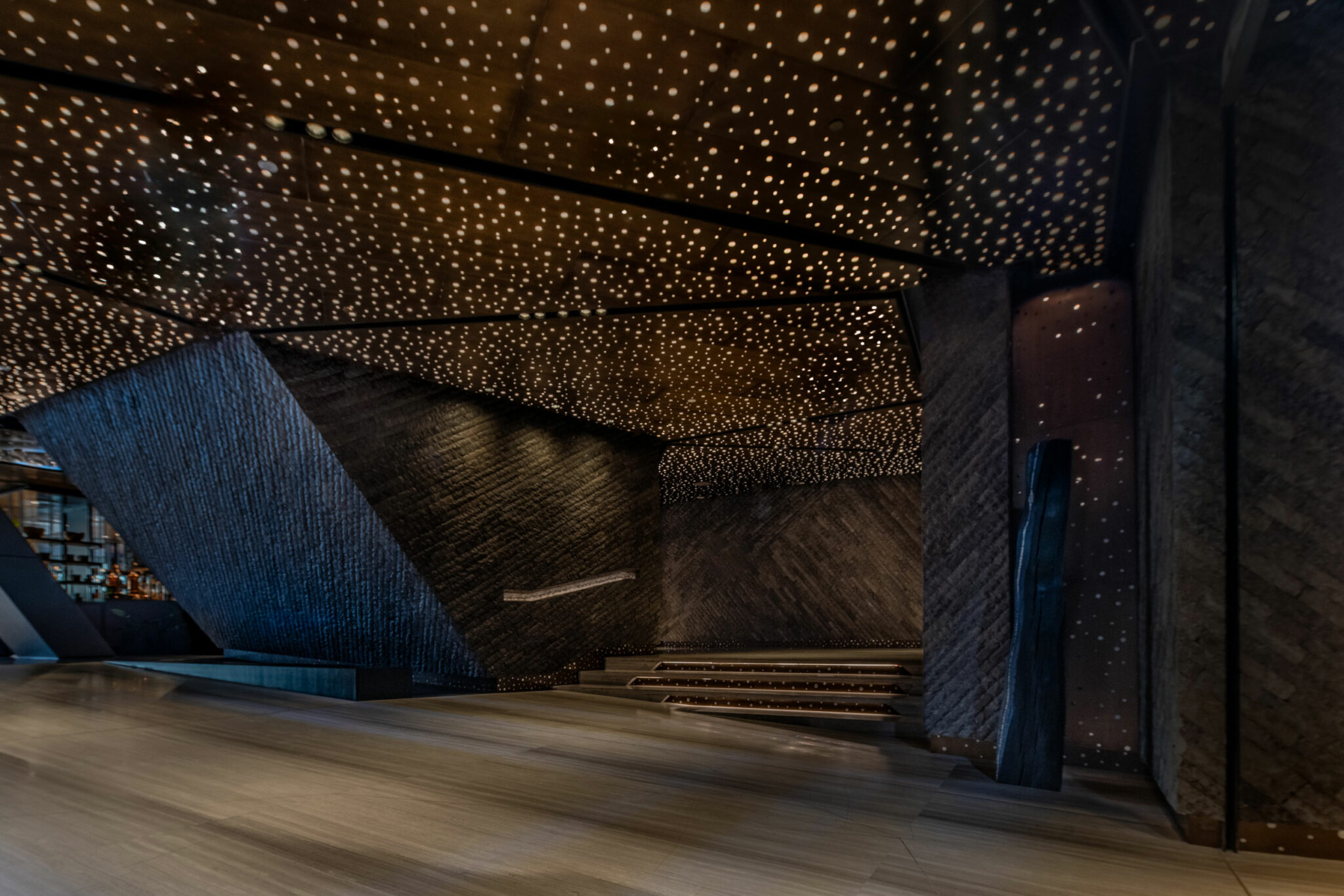 A luxurious, dimly lit restaurant lobby with textured dark stone walls and a ceiling dotted with small lights resembling stars, creating a serene, elegant ambiance.