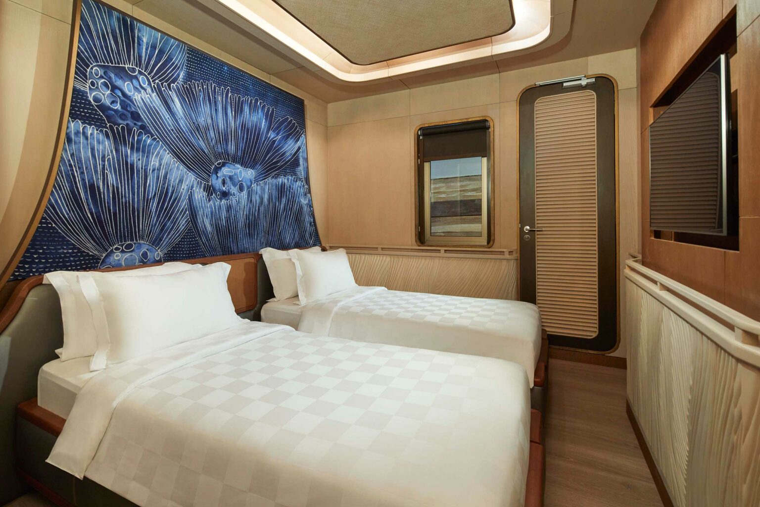 Modern yacht cabin with two single beds, white linens. A large blue abstract mural of flowers decorates the wall, creating a calming atmosphere.
