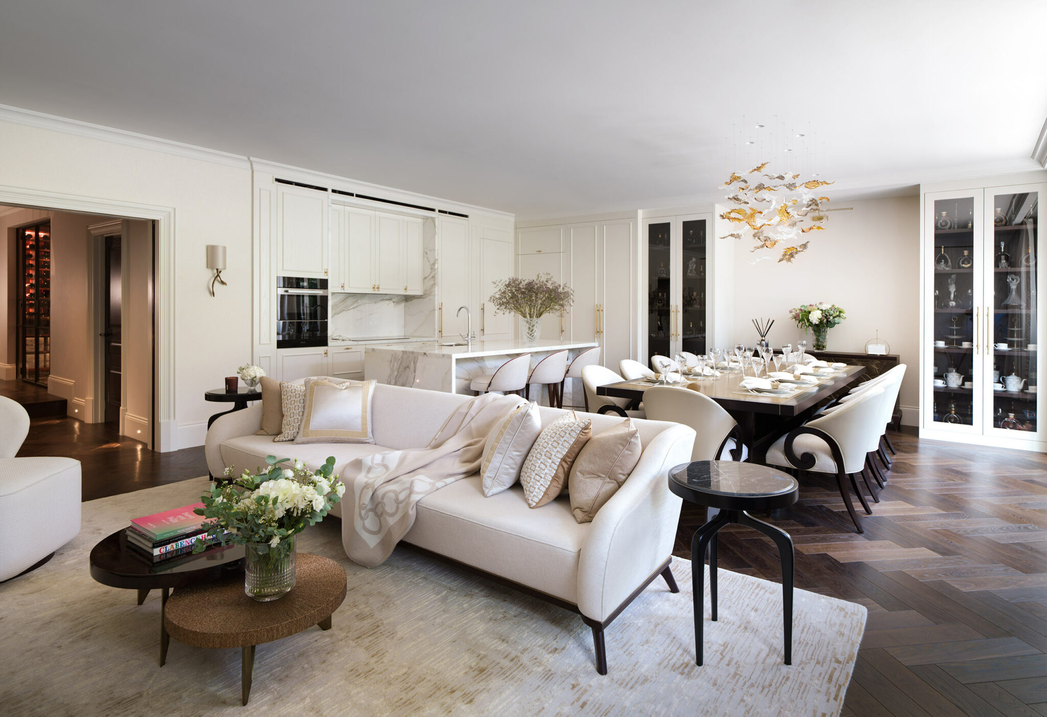 Elegant open-plan living and dining area with cream sofas, a wooden dining table set for guests, chic lighting, and a neutral palette, conveying sophistication.
