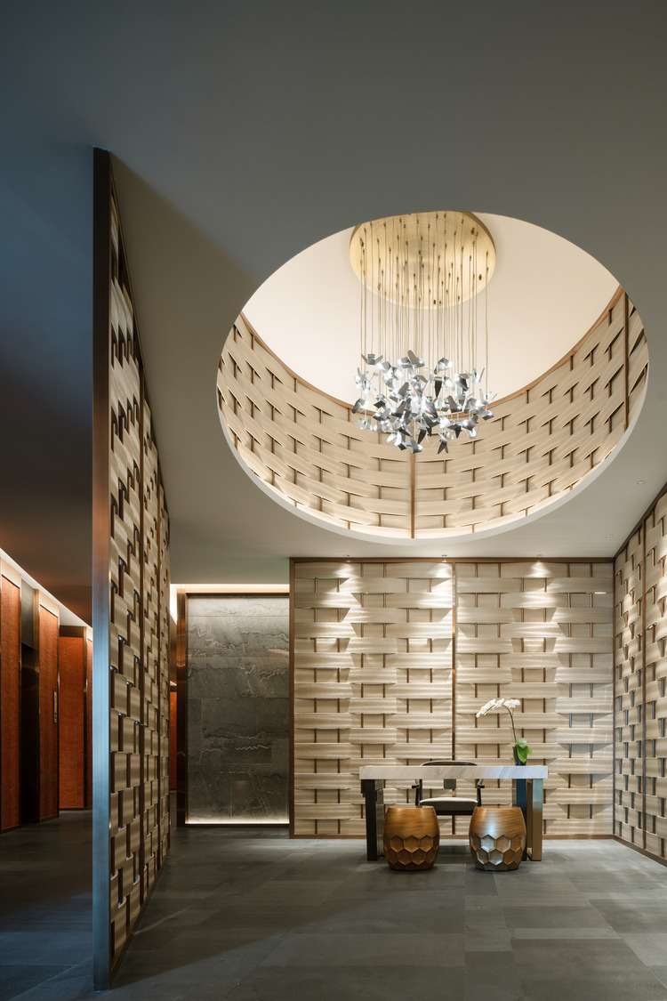 A contemporary restaurant entryway featuring textured wooden walls, a striking circular chandelier, and stylish accent tables, creating a welcoming and elegant atmosphere for guests in a luxury setting.