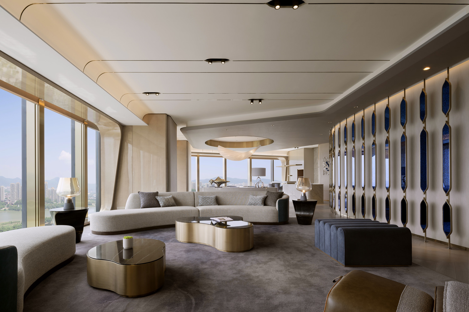 A luxurious suite living room featuring curved sofas, elegant lighting fixtures, and modern decor, with expansive windows offering breathtaking views, creating a sophisticated and inviting environment for relaxation.