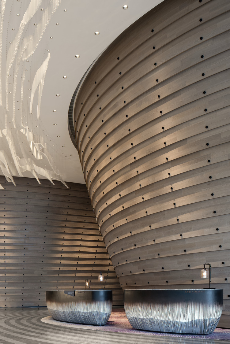 A striking hotel lobby with a curved wooden wall and elegant reception desks, enhanced by modern lighting, creating a welcoming and sophisticated atmosphere.