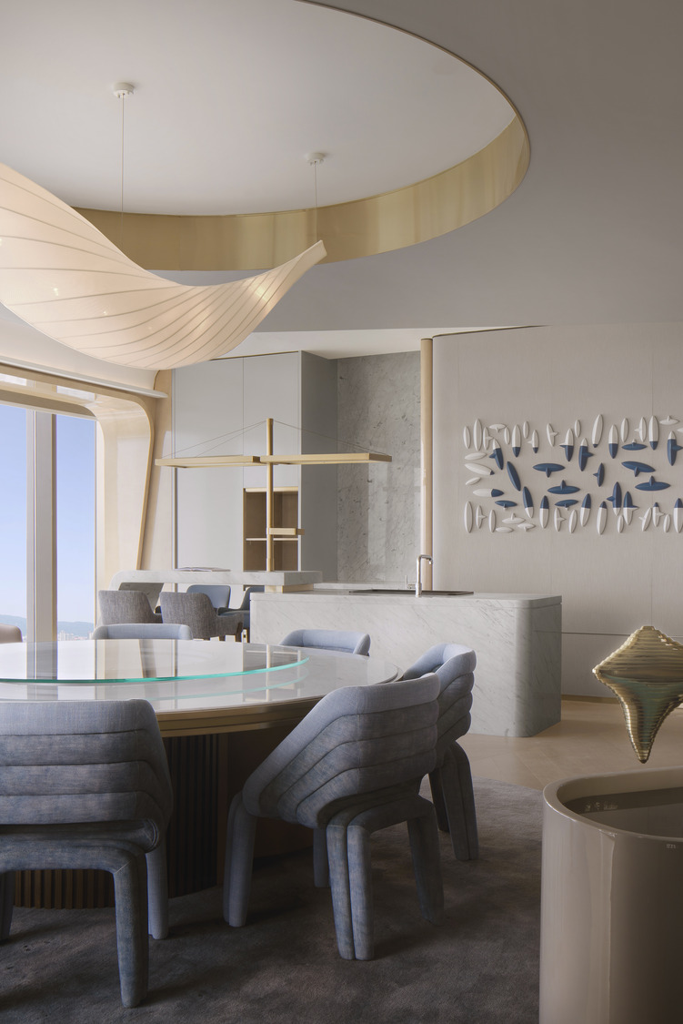 A modern luxury suite dining room with a round table and plush grey chairs. An elegant pendant light hangs above, complemented by contemporary wall art. Large windows provide stunning views, creating a sophisticated atmosphere for upscale dining in a high-end hotel.