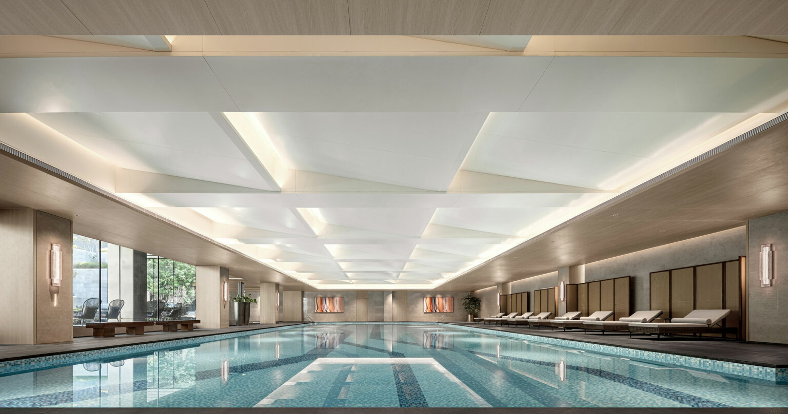 Luxurious indoor pool area with a geometric-patterned ceiling and tranquil lighting. Poolside lounge chairs line the serene space, offering a relaxing ambiance.