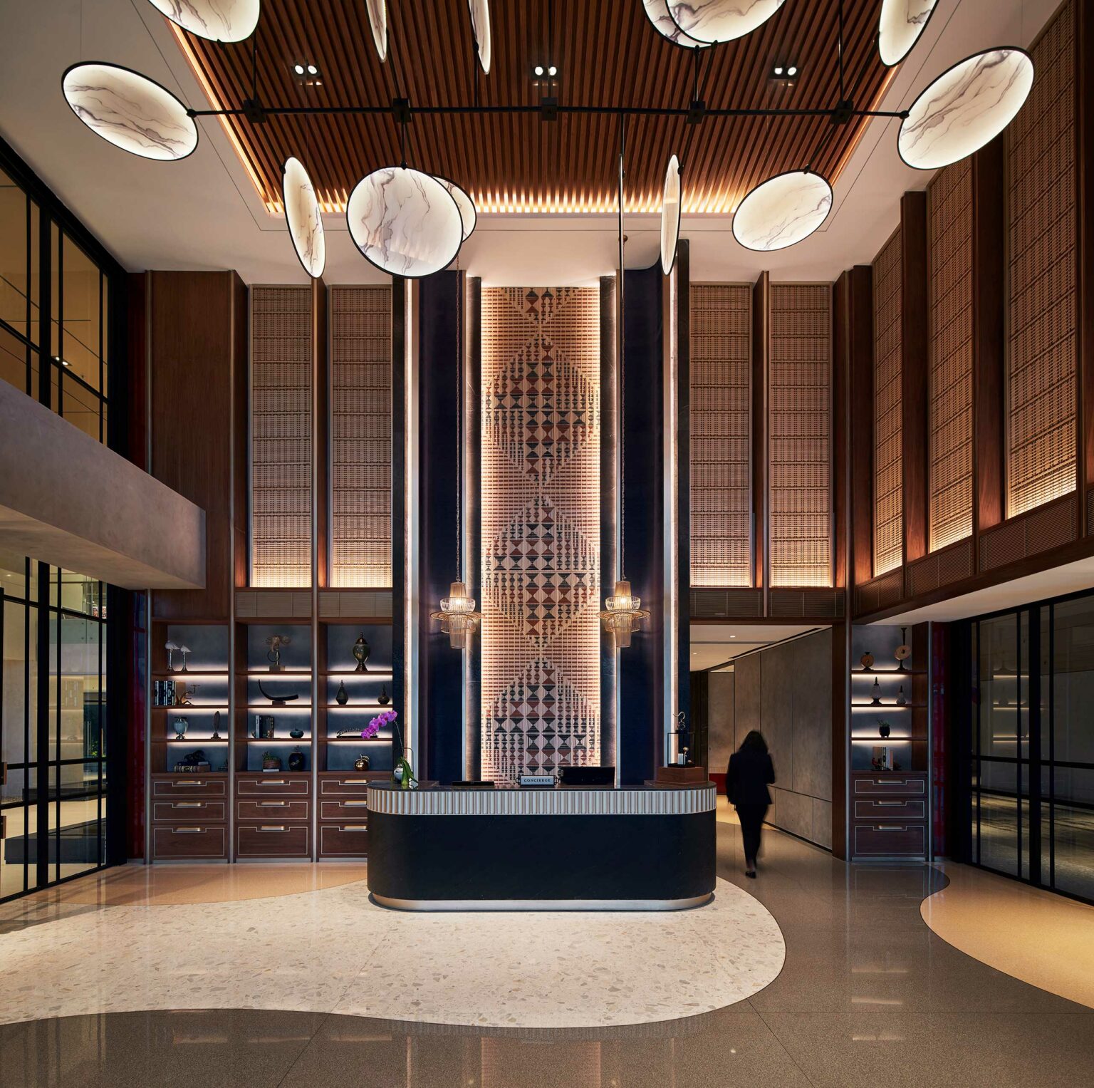 Luxurious hotel lobby with a modern, elegant design. Features a marble-topped reception desk, large ornate wall pattern, and ambient lighting.