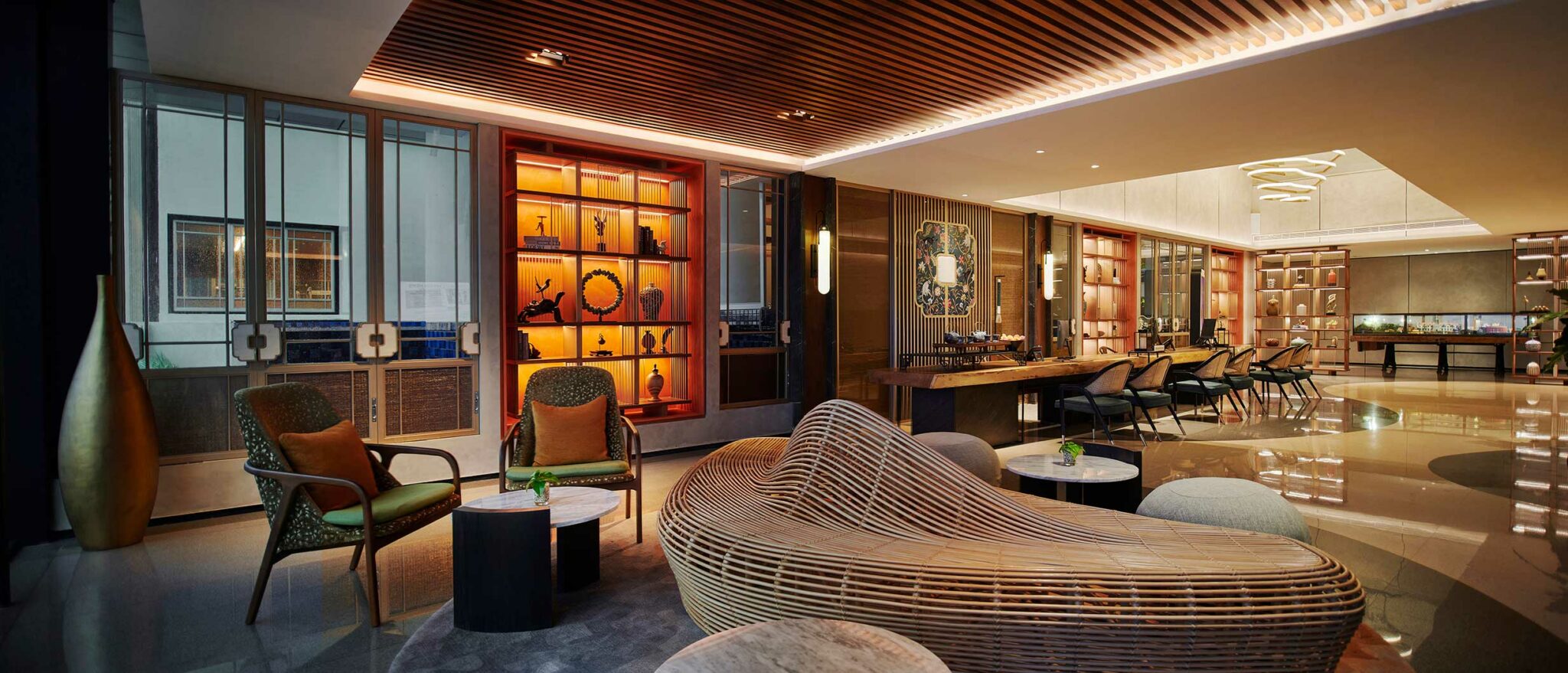 Modern hotel lounge area with warm lighting, wooden accents, and contemporary furniture, including artistic wooden seating and a decorative backlit shelf.