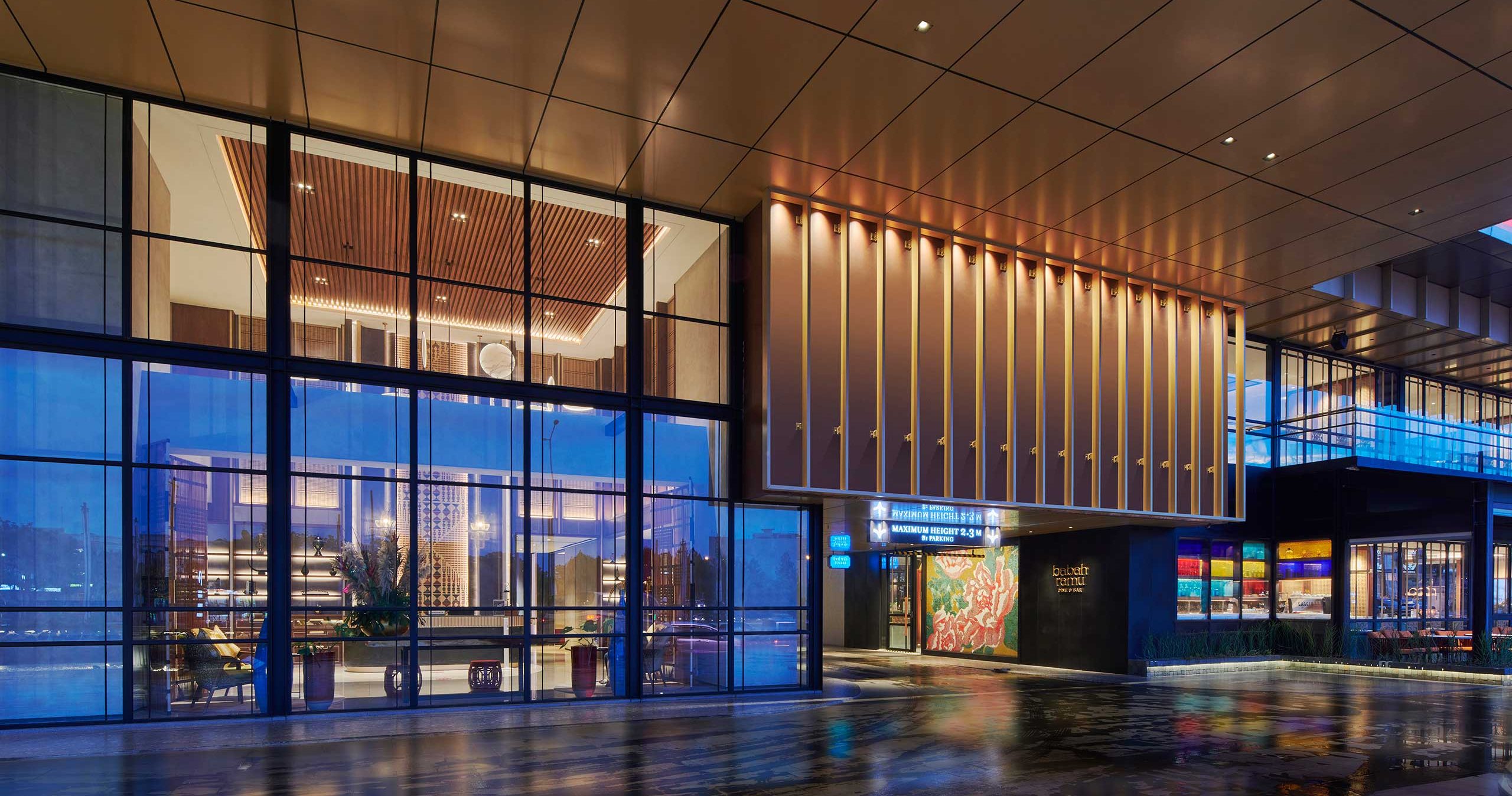 A modern hotel entrance at dusk with large glass windows, warm lighting, sleek architectural lines, and an inviting, luxurious atmosphere.