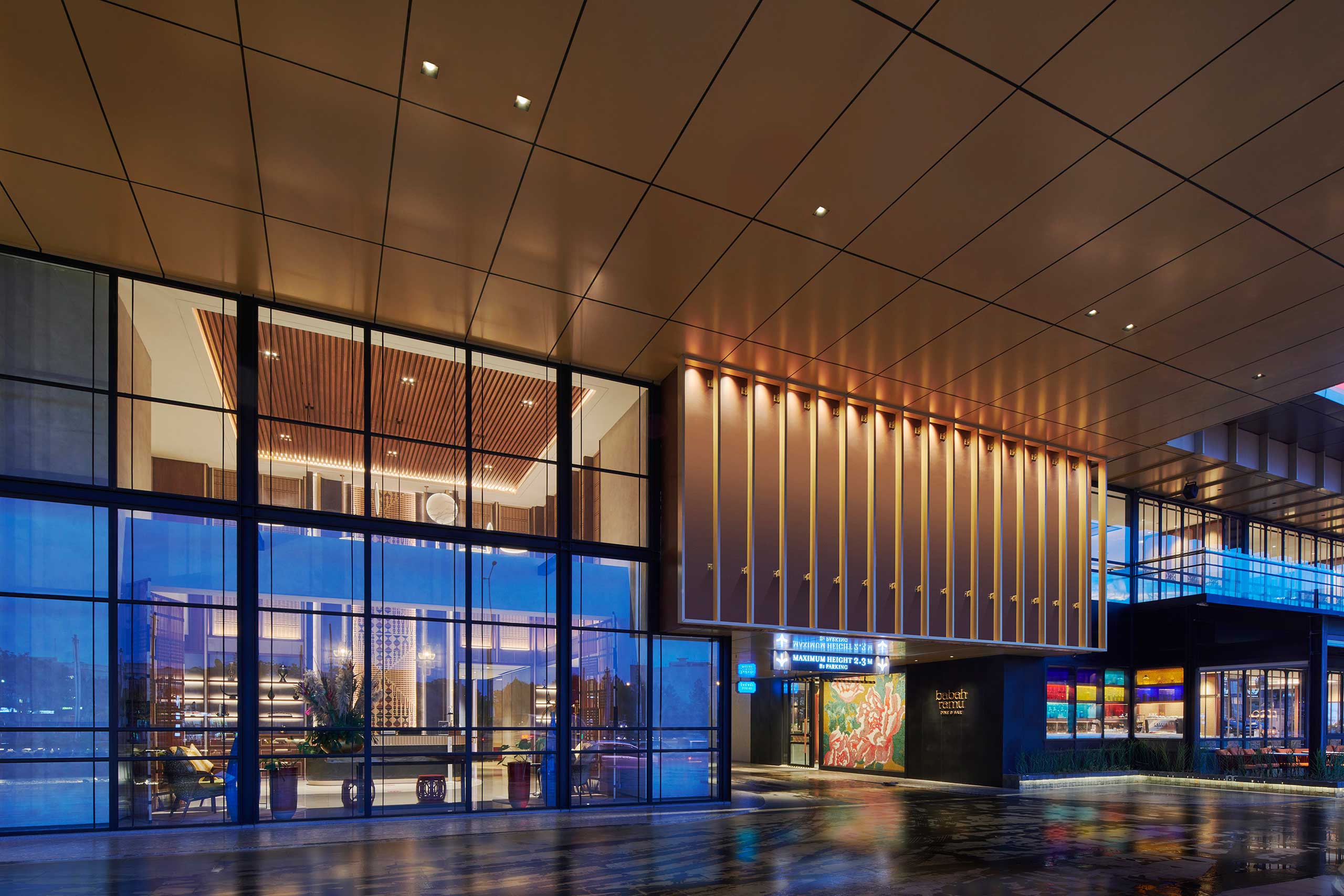 A modern hotel entrance at dusk with large glass windows, warm lighting, sleek architectural lines, and an inviting, luxurious atmosphere.