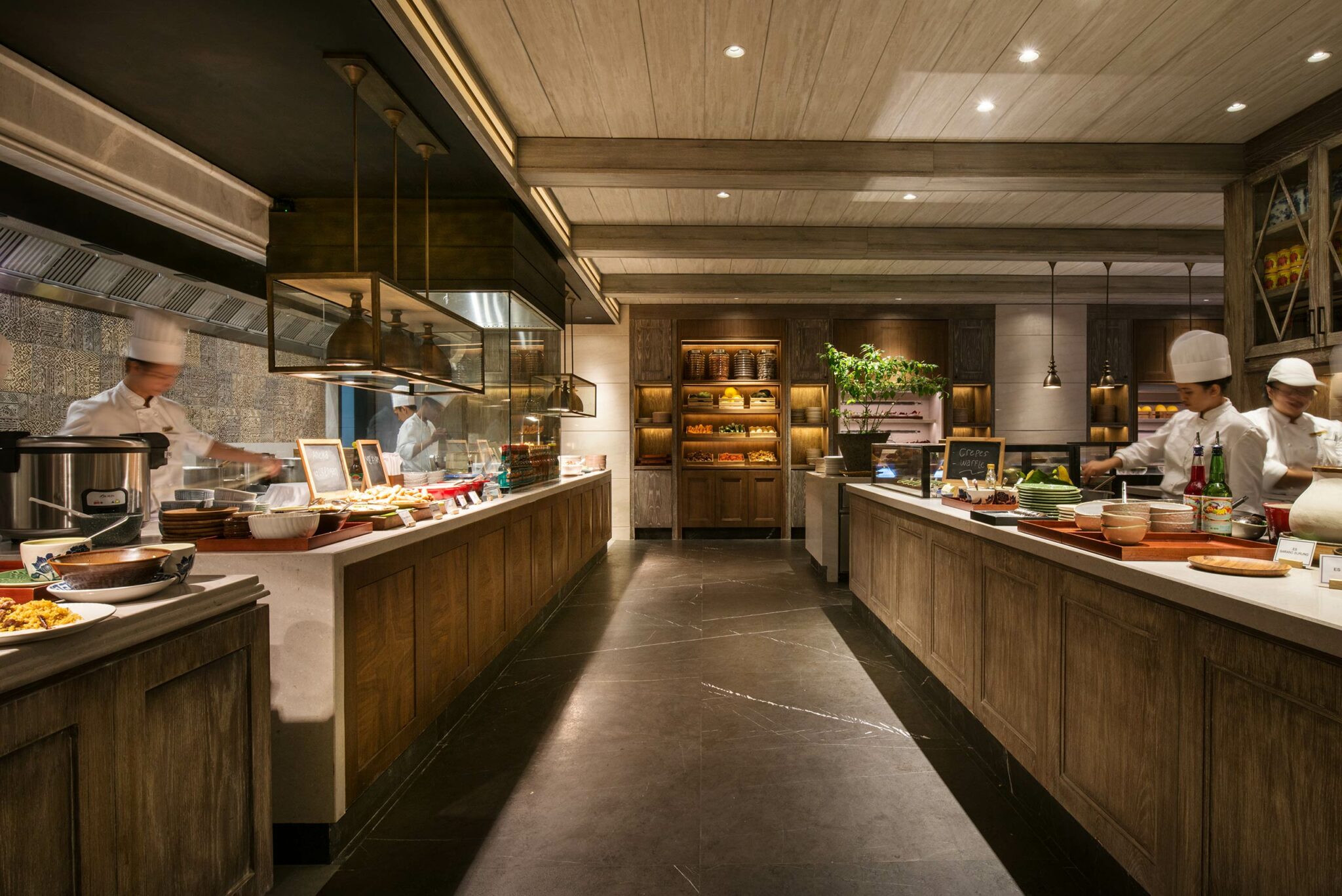 A spacious restaurant kitchen showcases chefs in white uniforms and hats preparing dishes. The warm lighting and wood accents create an inviting atmosphere.