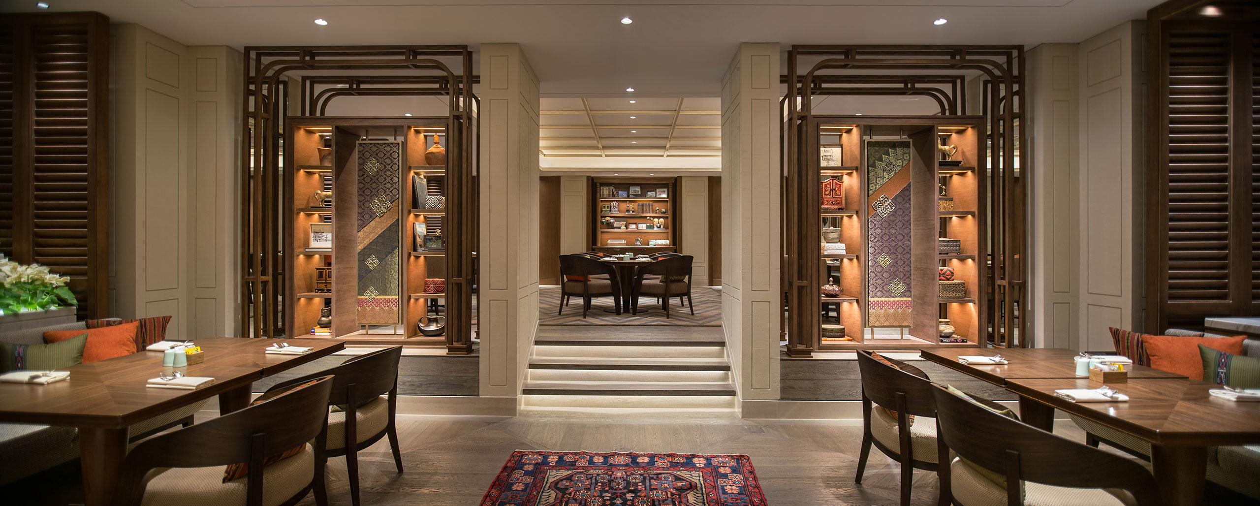 Elegant restaurant interior with warm lighting, showcasing wooden shelves with books and decor. Central focus on two tables set for dining. Cozy ambiance.