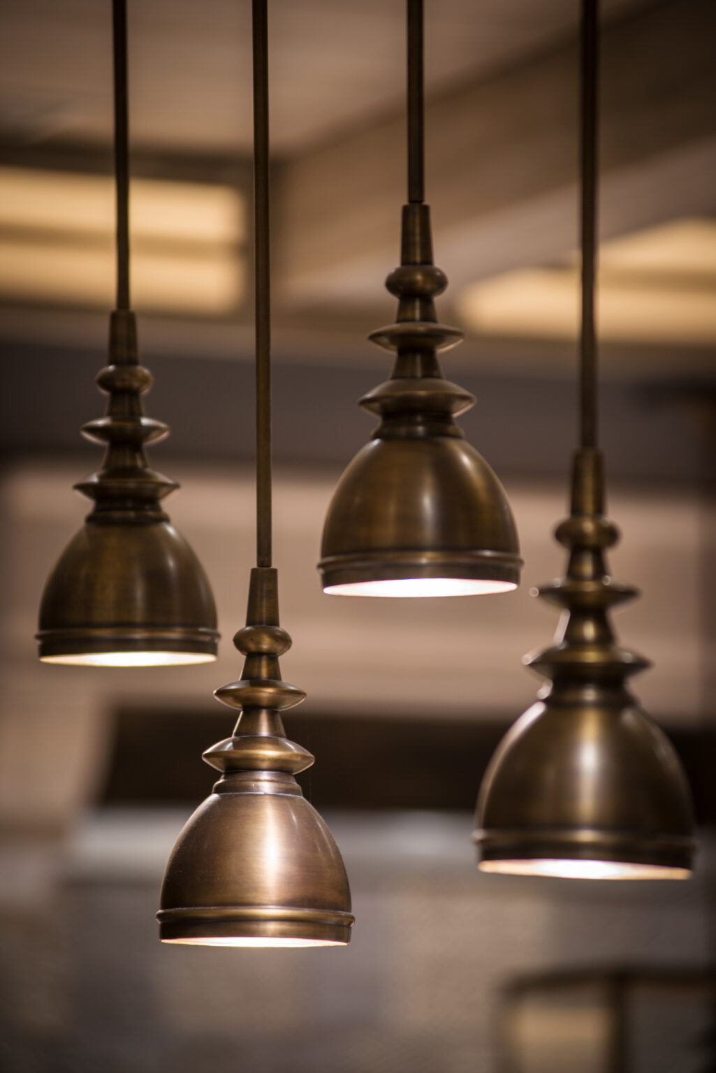 Close-up of four vintage bronze pendant lights hanging from the ceiling, casting a warm glow. The lights create a cozy, inviting atmosphere.