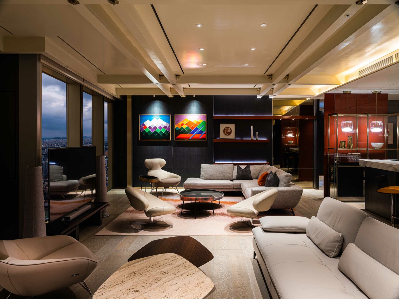Modern suite living room with sleek furniture, abstract art on the wall, and a large window showing a city view. The atmosphere is cozy and sophisticated.