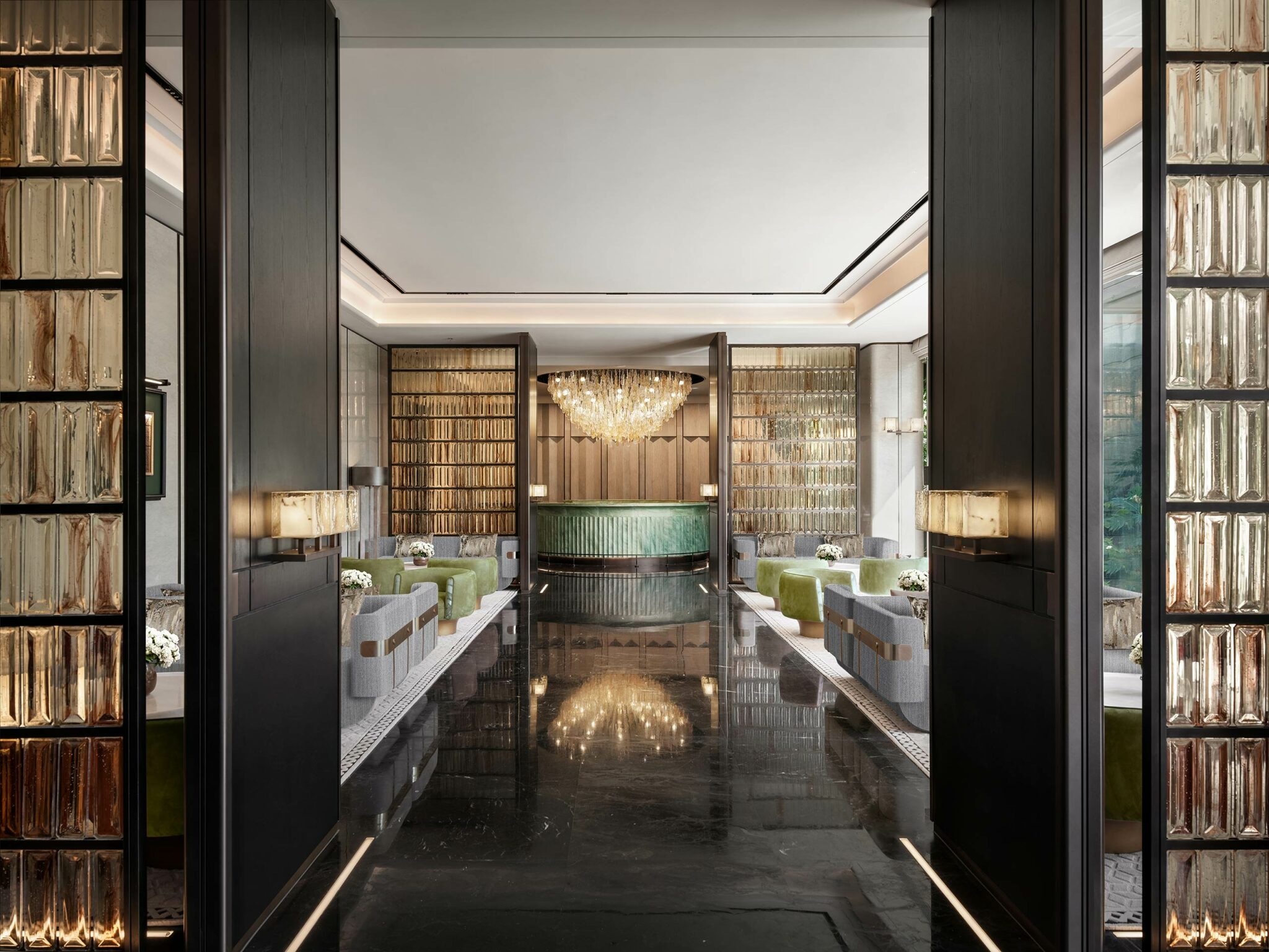 Luxurious hotel lobby with modern design, featuring a large central chandelier, glossy black floors, green seating, and wooden accents, exuding elegance.