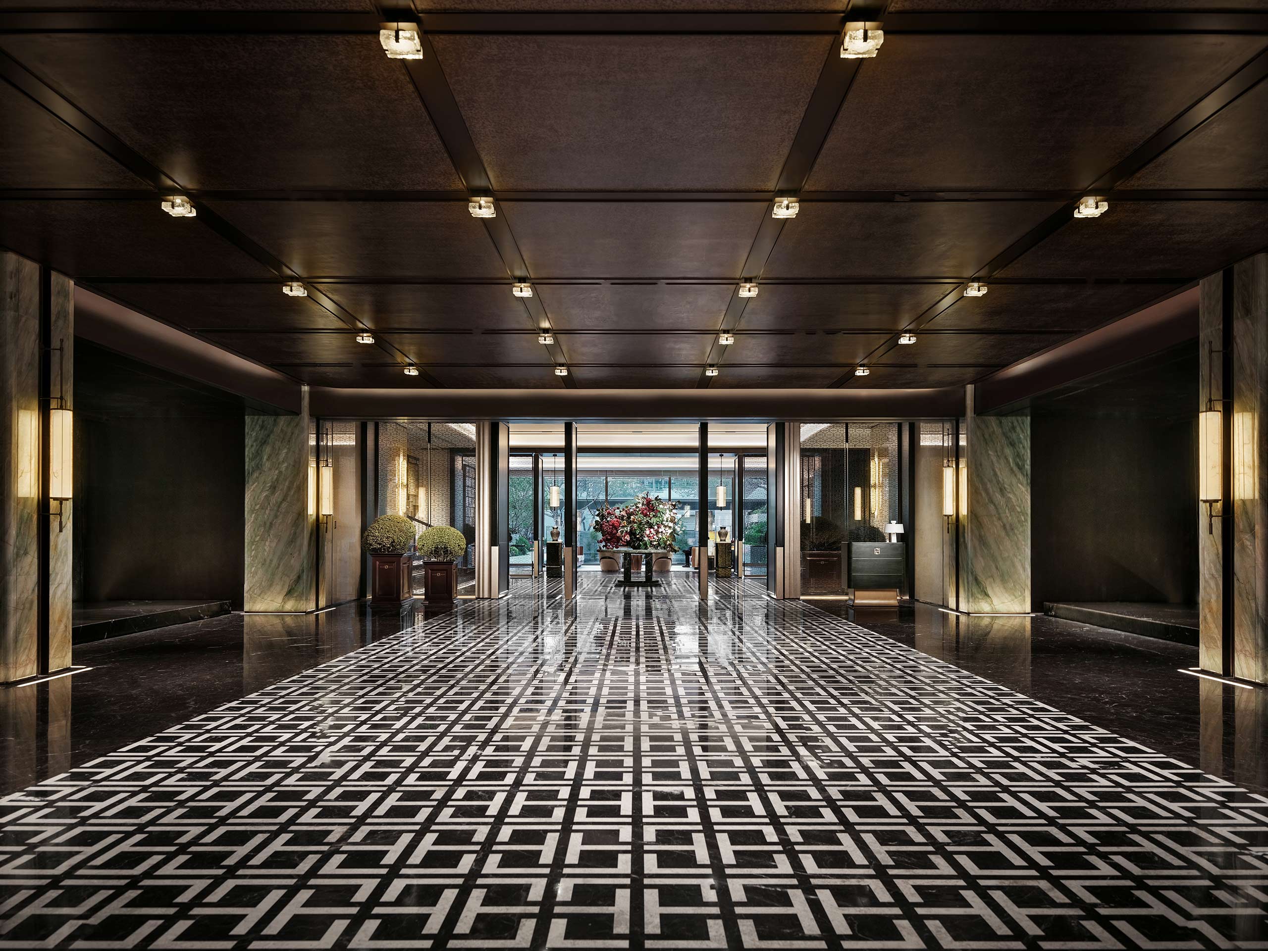 Luxurious hotel lobby with geometric black-and-white tiled floor, modern lighting, and a large floral centerpiece. Elegant and inviting atmosphere.